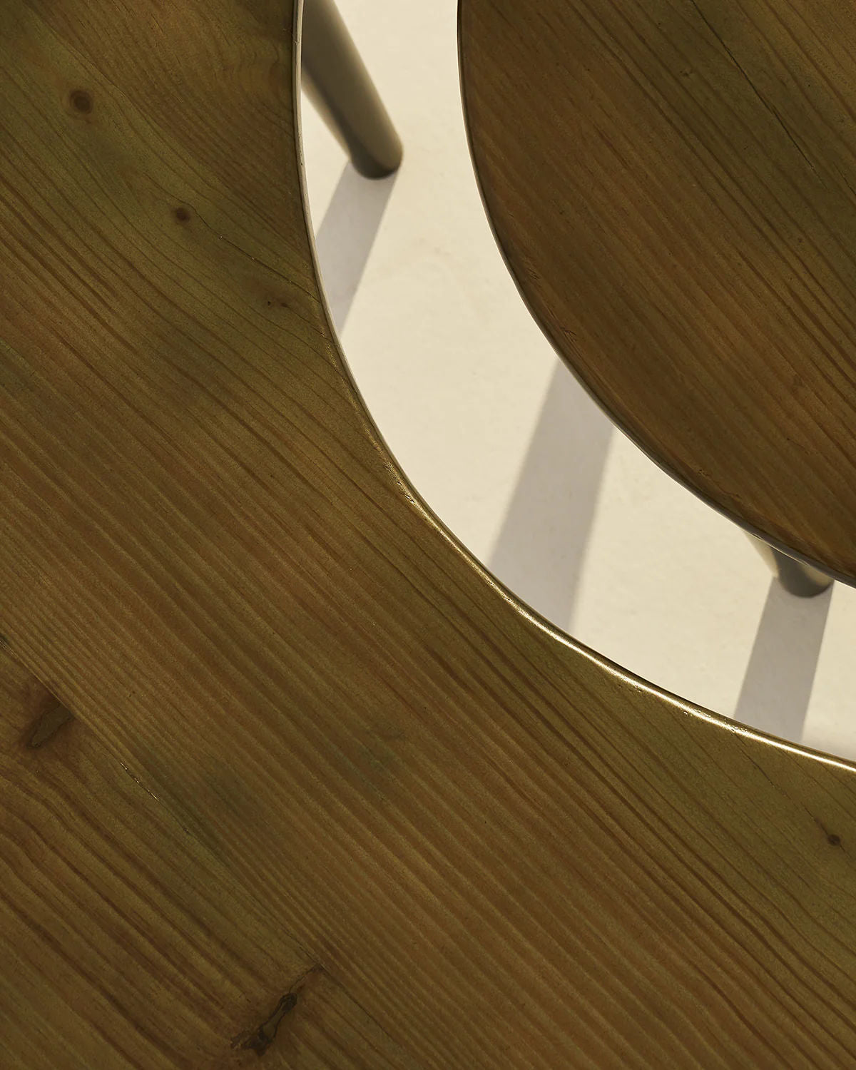 Close-up of the Crescent Coffee Table Set of 2 by LMNOH: two overlapping crescent-shaped tables casting shadows. The larger ashwood table has a smooth finish and visible grain; the smaller, partially visible, offers similar texture and space-saving functionality.