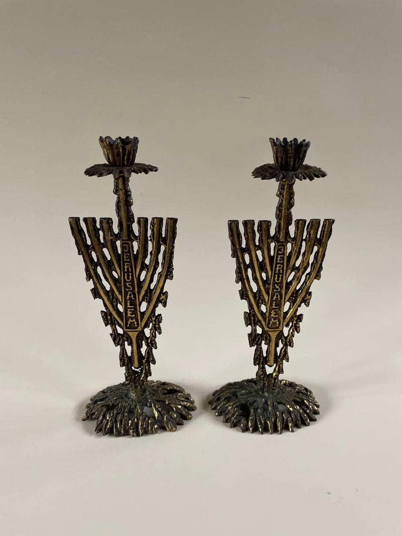A pair of Brutalist Metal Candleholders by Maud Vaughan from the 1970s stands on a flat surface, showcasing intricate detailing. These vintage pieces feature vertical brutalist-inspired designs with "Jerusalem" inscribed vertically on each holder, complemented by textured and elaborate bases that enhance their charm and character.