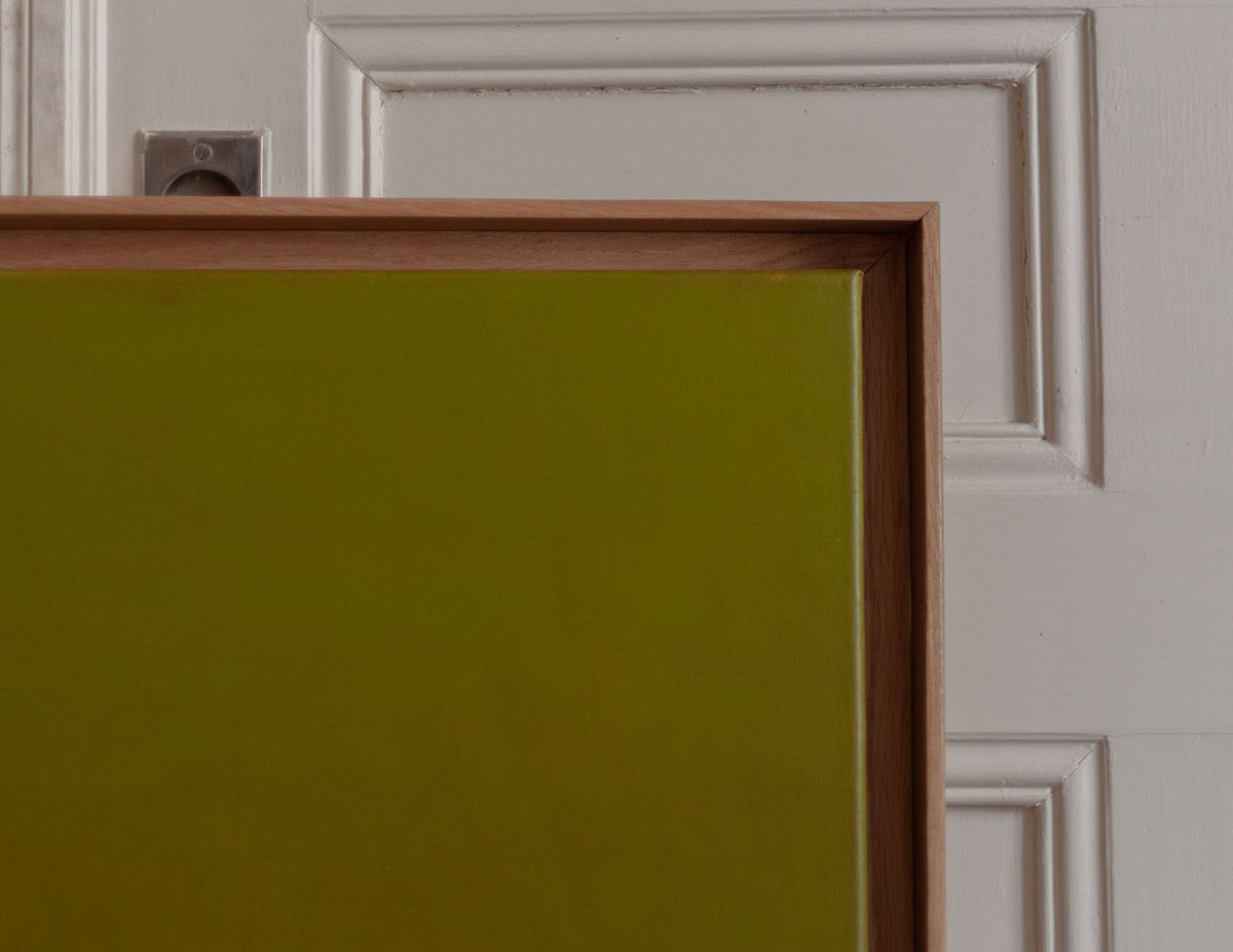 A close-up of a framed Thru and Thru #2 green acrylic painting by Rebecca von Matérn, mounted in a brown wooden frame, leaning against a white paneled door. The focus is on the texture and color contrast between the items.