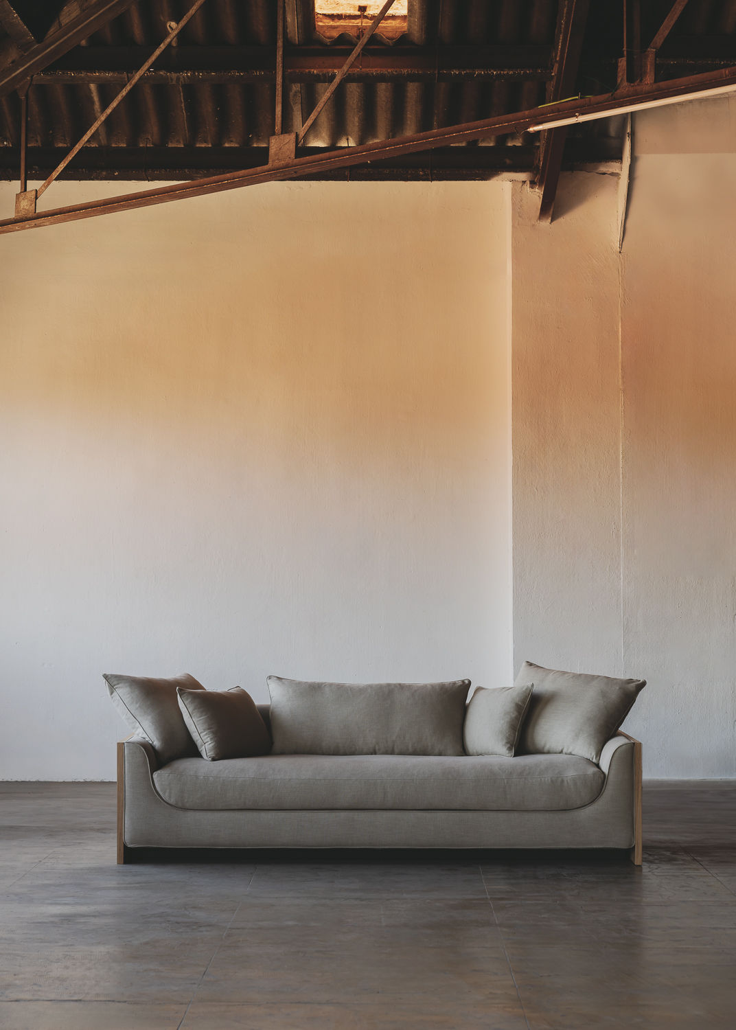 The ASERIES OF OBSTACLES, SL Marina Sofa, with removable backrests, provides plush comfort in an industrial-style space. Its modern gray look complements gradient walls from white to beige, while the exposed ceiling and concrete floor add to the minimalist vibe. A solid oak frame ensures durability.