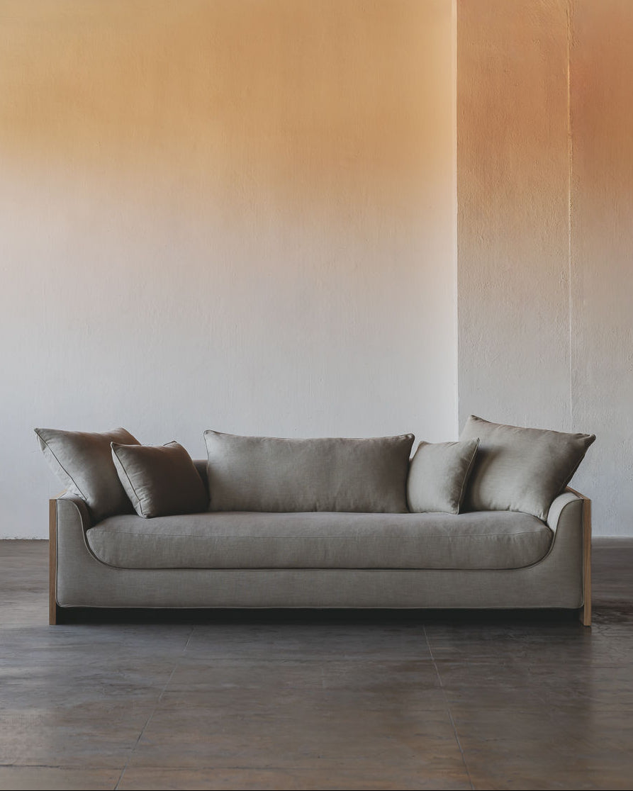 The ASERIES OF OBSTACLES, SL Marina Sofa, with removable backrests, provides plush comfort in an industrial-style space. Its modern gray look complements gradient walls from white to beige, while the exposed ceiling and concrete floor add to the minimalist vibe. A solid oak frame ensures durability.