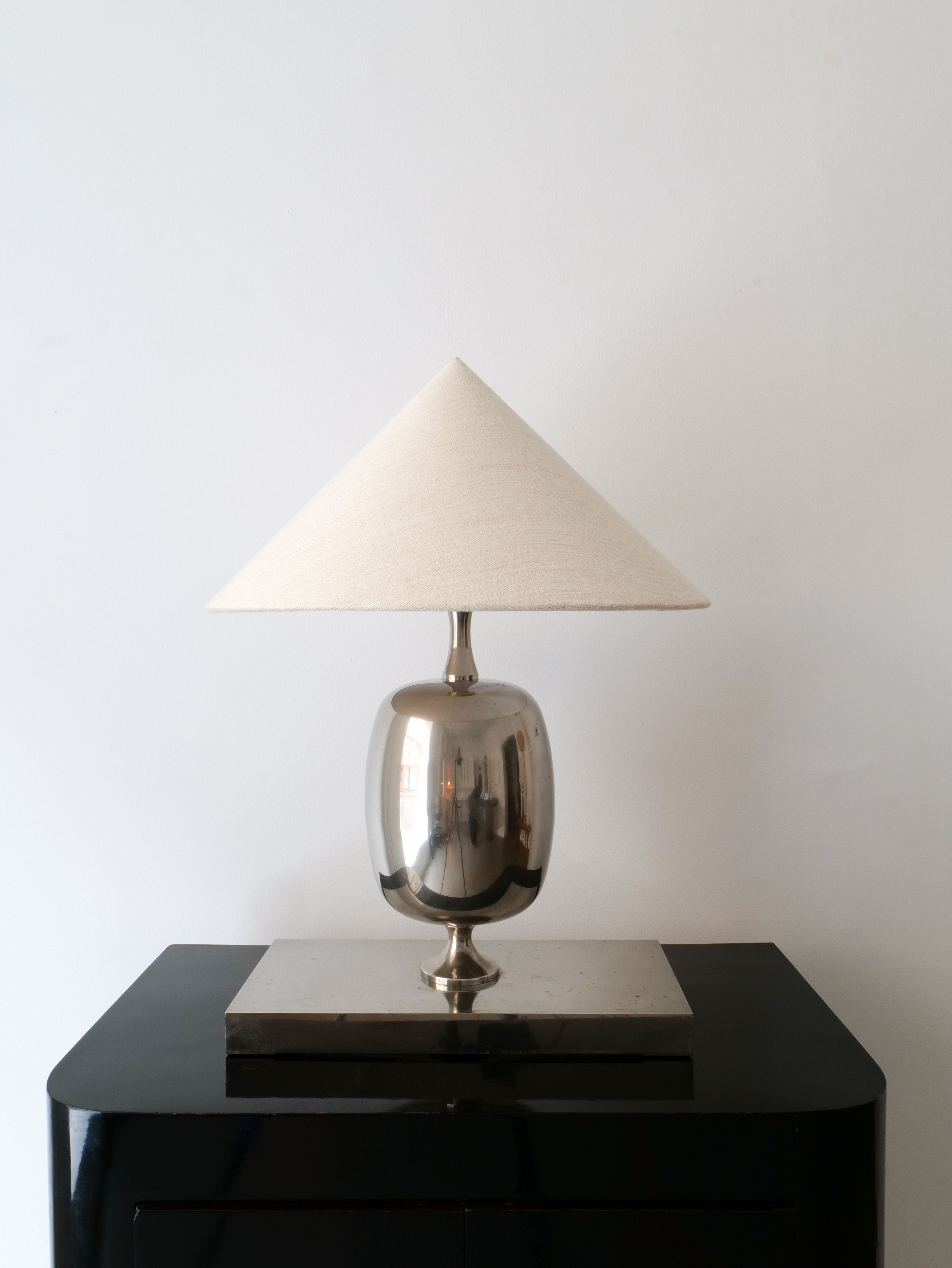 The Barbier Chrome Table Lamp by Collection apart shines with its chrome over brass base under a white conical shade, elegantly positioned on a black rectangular surface against a simple white background.