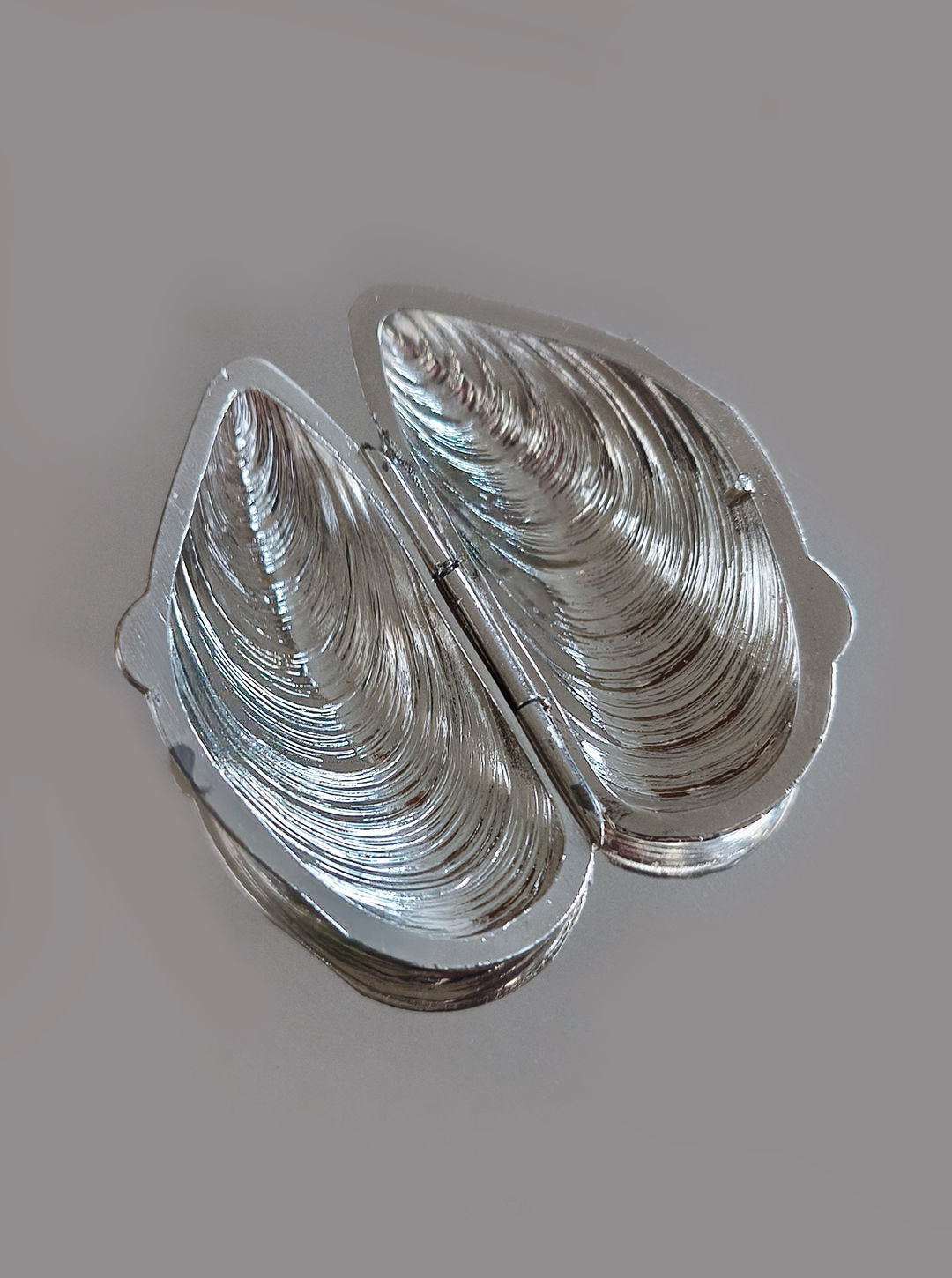 Les Objoies' Small Shell Box earrings feature a compact, textured silver design resembling mussel shells, hinged at the center for stylish elegance on any occasion. Displayed against a plain background.