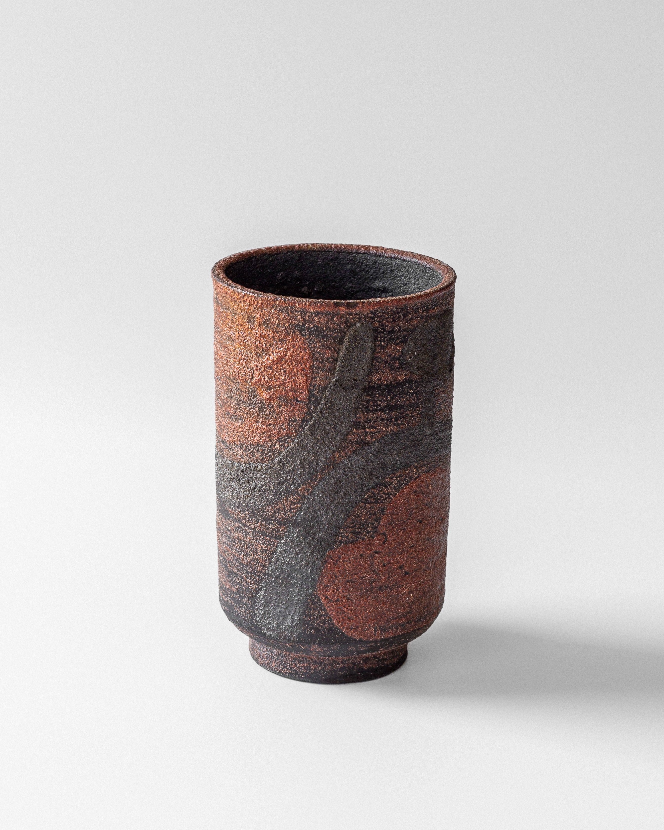 The Modernist Vase by Jaap Dommisse, from Spigel, is a textured cylindrical piece featuring an earthy rough surface with abstract patterns in avant-garde ceramics style. Shades of brown and gray create a striking contrast against the white background.