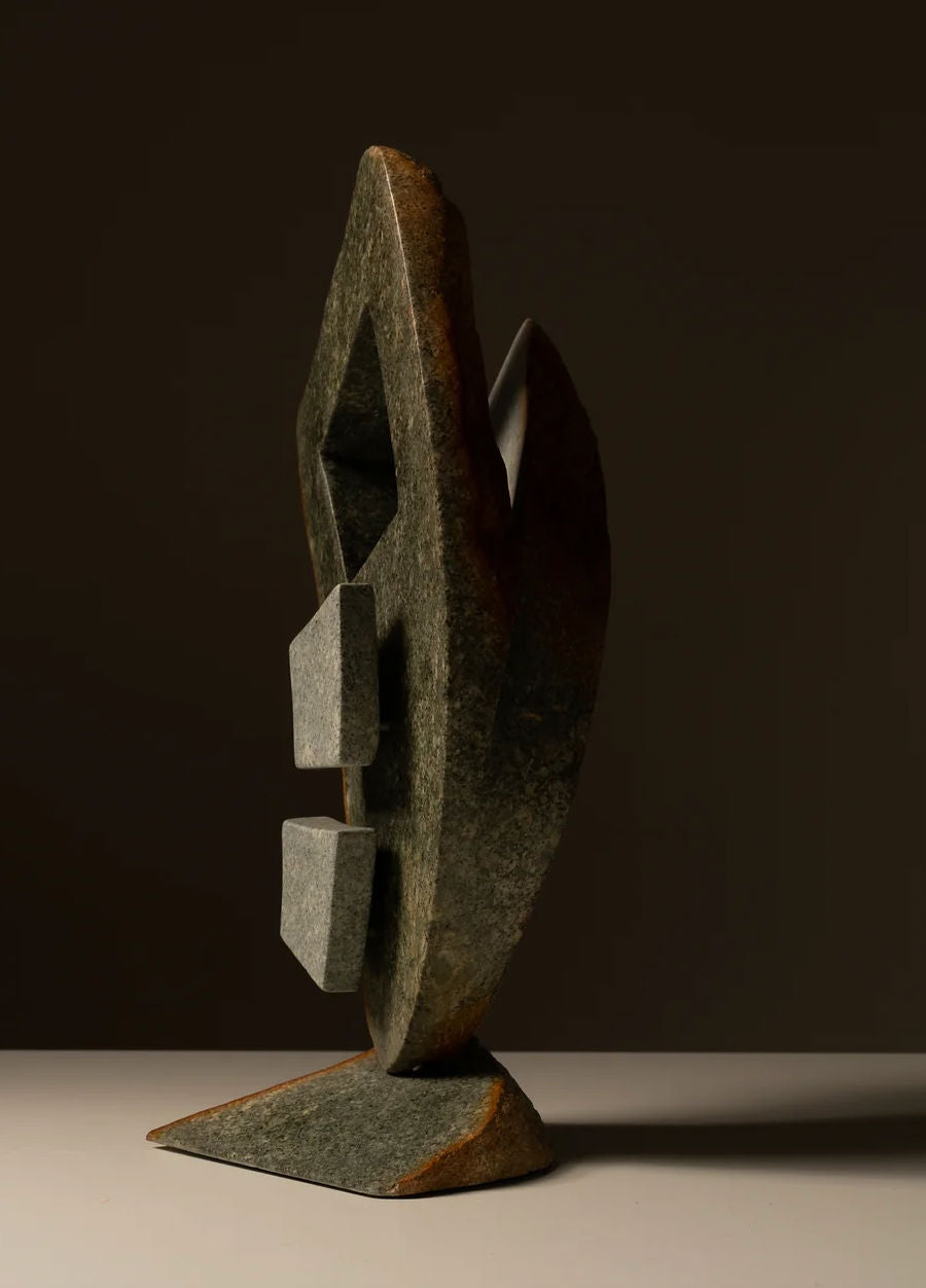 The handcrafted Two-toned Abstract Sculpture by Les Objets Amsterdam features geometric stone shapes, including two rectangular protrusions and a diamond-shaped hole, standing on a triangular base against a brown backdrop, casting an intriguing shadow.