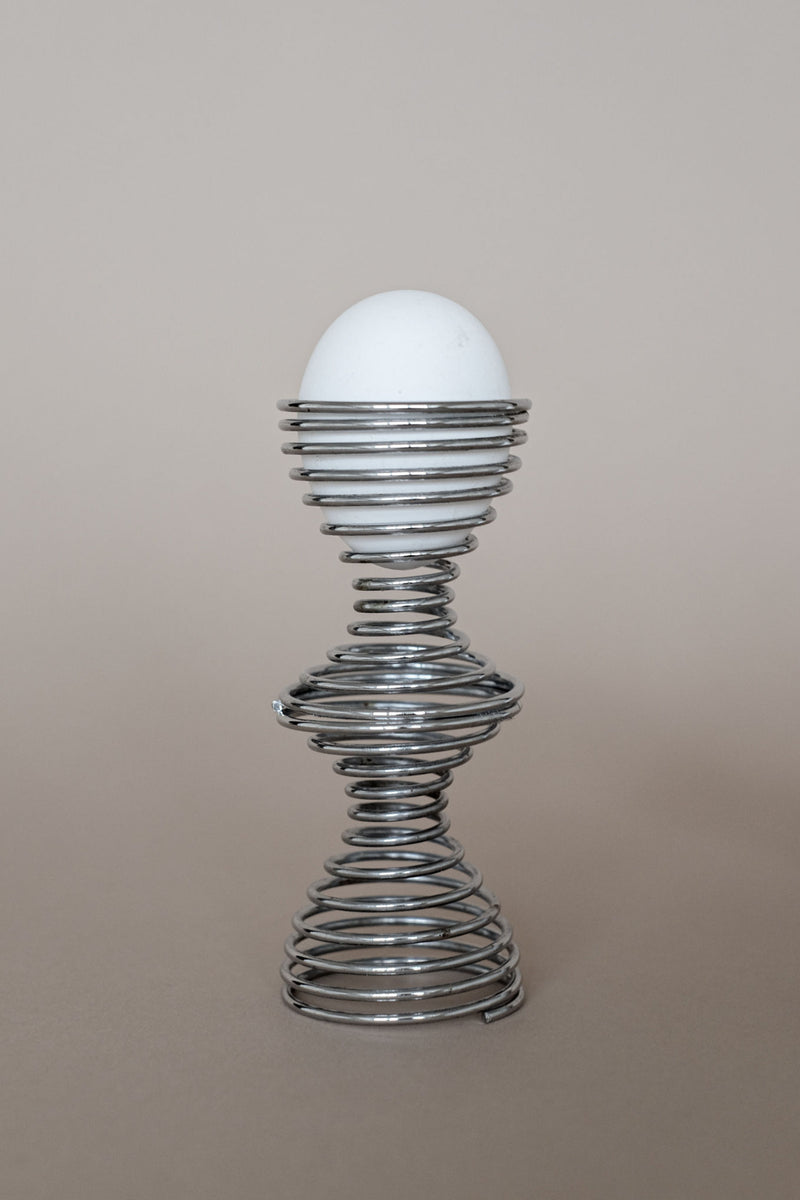 Modern wire spiral egg cup holding white egg on neutral background