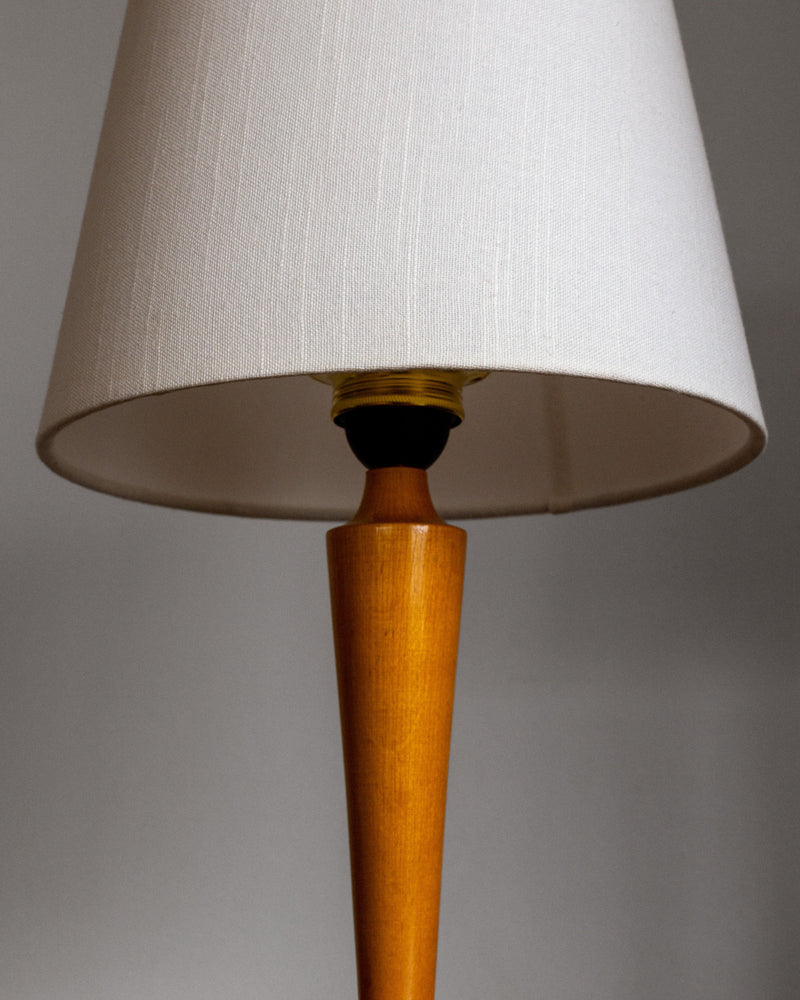 A close-up of the Spigel 1930s Swedish Birch Table Lamp, featuring a wooden base and white fabric lampshade, set against a plain gray background.