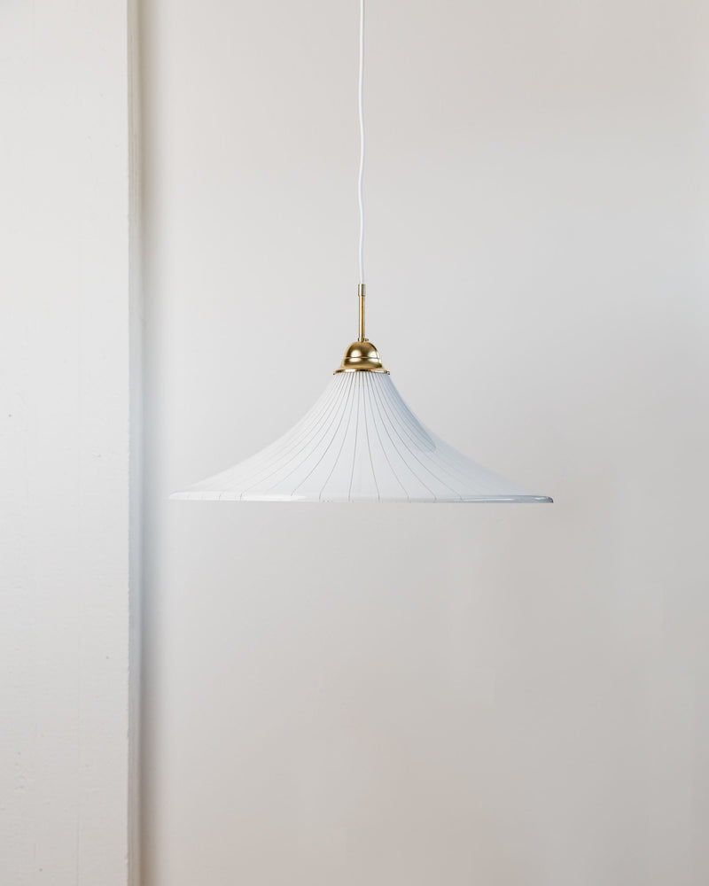 Suspended from a white cord against a minimal light-colored wall, the Bottega Jacobs "Ceiling Lamp 1970s Italy" showcases a single pendant light with a wide, white pleated shade and brass detailing, exuding the charm of an XL vintage ceiling lamp inspired by 1970s design.