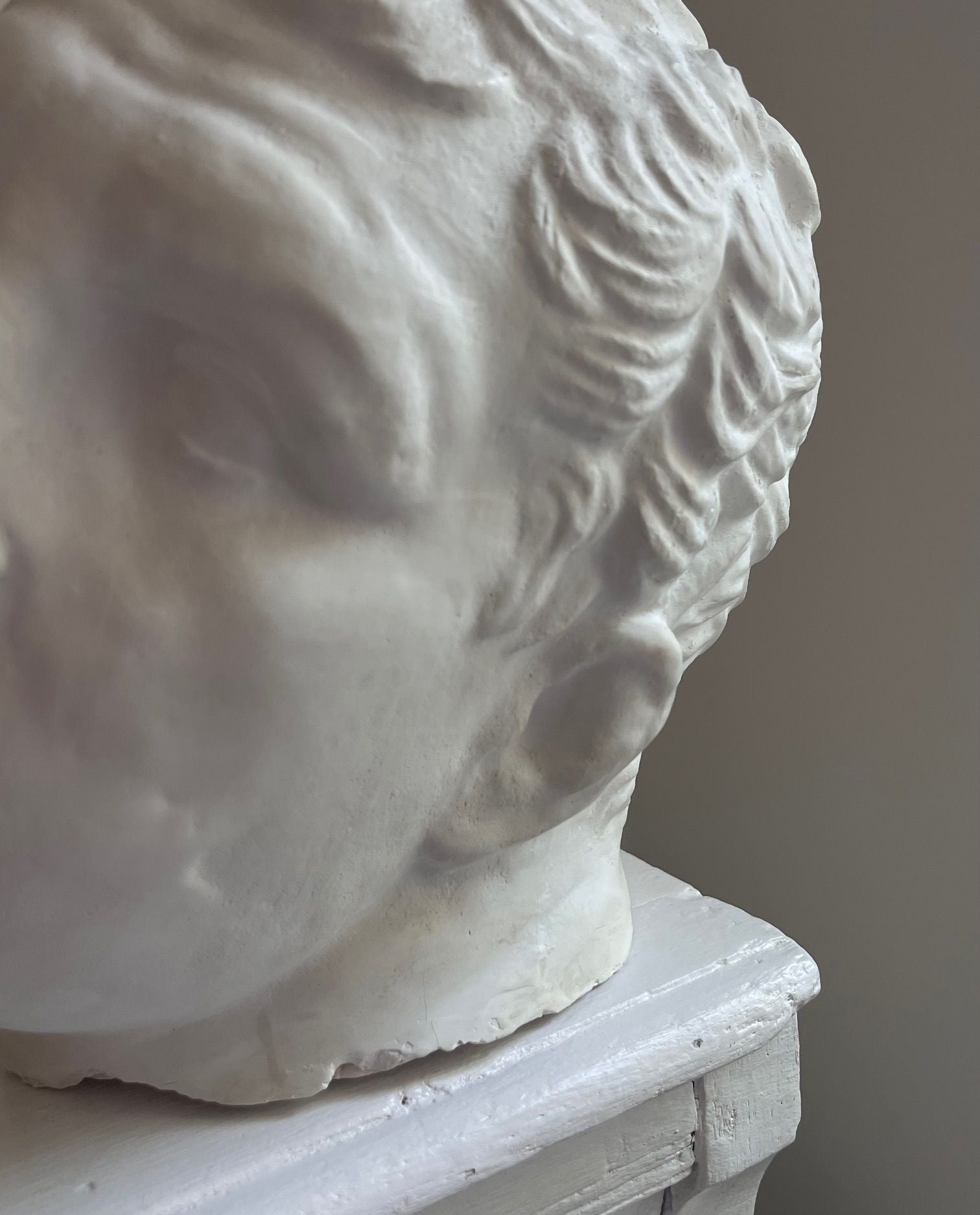 Close-up of an Italian Male in Plaster by Médecine, featuring the side profile of a person's face. The image highlights the intricate details of the hair, ear, and part of the visage, which appears smooth and finely sculpted. This vintage design bust is showcased on a white surface.