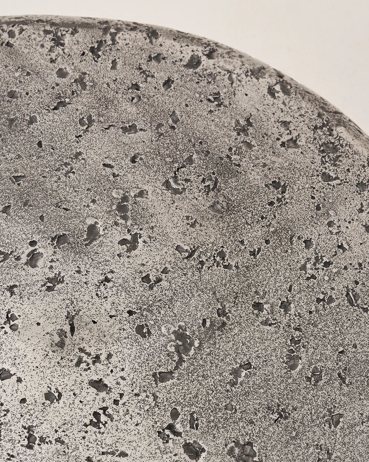 The Crater - Set of 2 by LMNOH features a textured surface similar to rough stone or concrete. Its gray tones and speckled indentations evoke a lunar landscape, creating an intriguing celestial centerpiece for any modern interior.