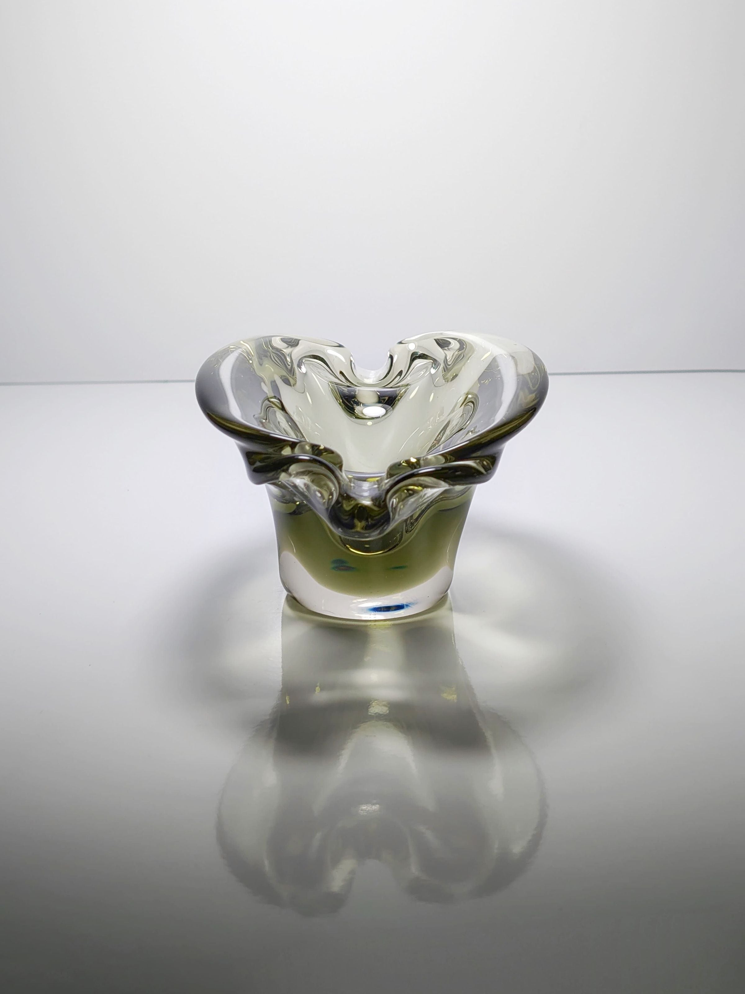 The Bohemian Smoked Glass Ashtray by Jan Beránek, a 1960s Dodo Vintage piece, features a clear wavy-edged design. Its smooth flow channels the era's essence, creating captivating reflections on its reflective surface and enhancing its elegant appeal.