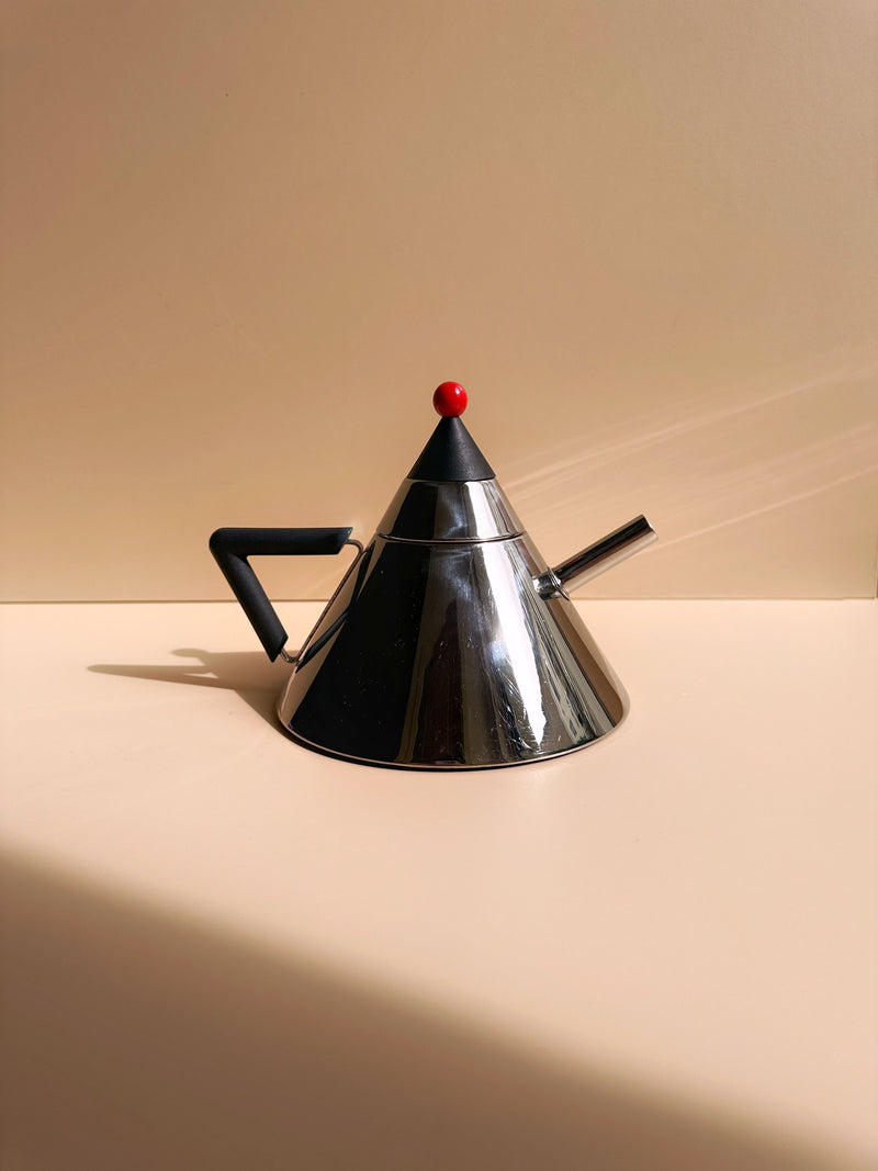The Japanese Postmodern Steel Tea Pot by Dodo Vintage features a conical stainless steel design with a black handle and spout, accented by a red ball atop the lid. Embodying postmodern design, it sits on a light-colored surface against a light tan background as steam gently rises from the spout.