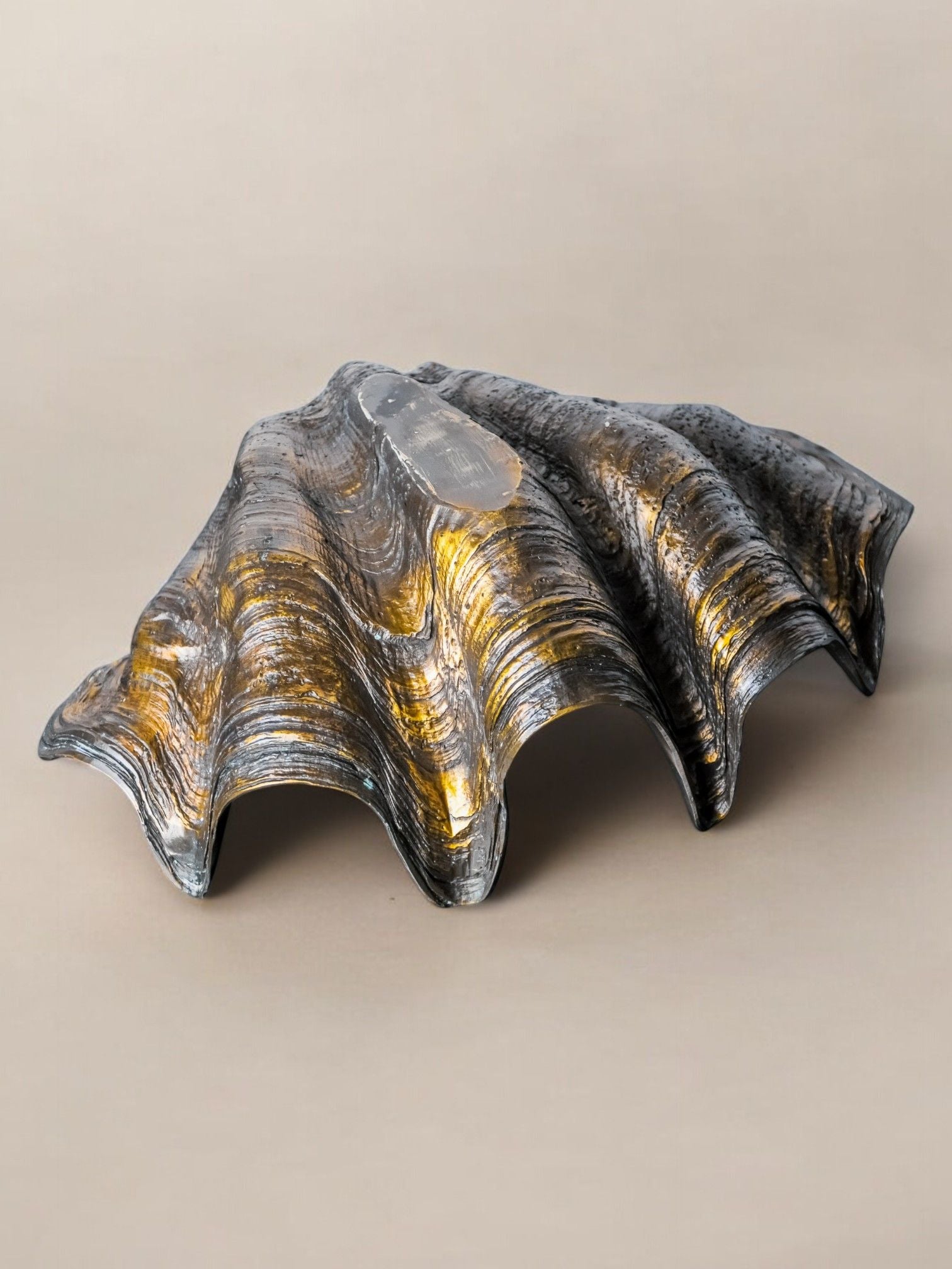 A large plaster sculpture crafted to resemble a designer scallop shell, featuring intricate layered textures. Designed by Malamar Studio in Italy during the 70s, it showcases a reflective metallic finish with shades of silver and gold against a plain backdrop.