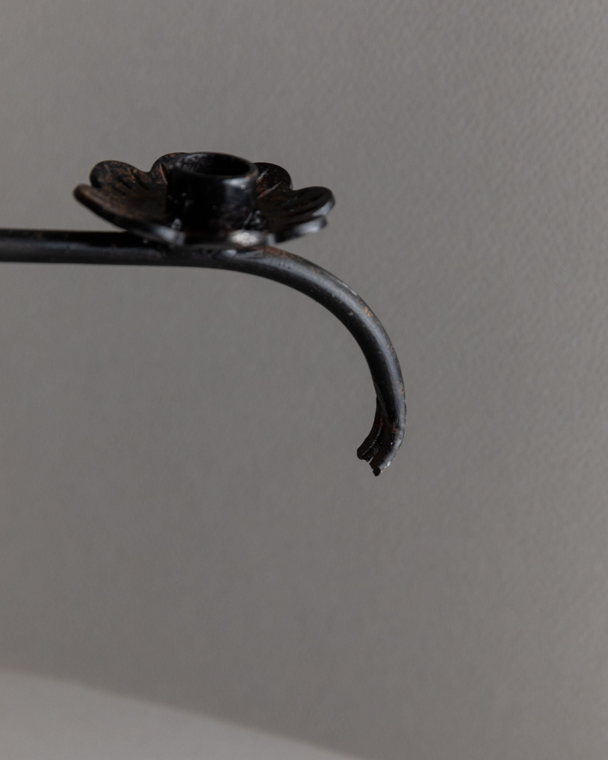 Close-up of the Bottega Jacobs Iron Candleholder, Italy 1960s, featuring a black metal hook with a curved end and flower detail reminiscent of vintage craftsmanship, set against a plain gray background.