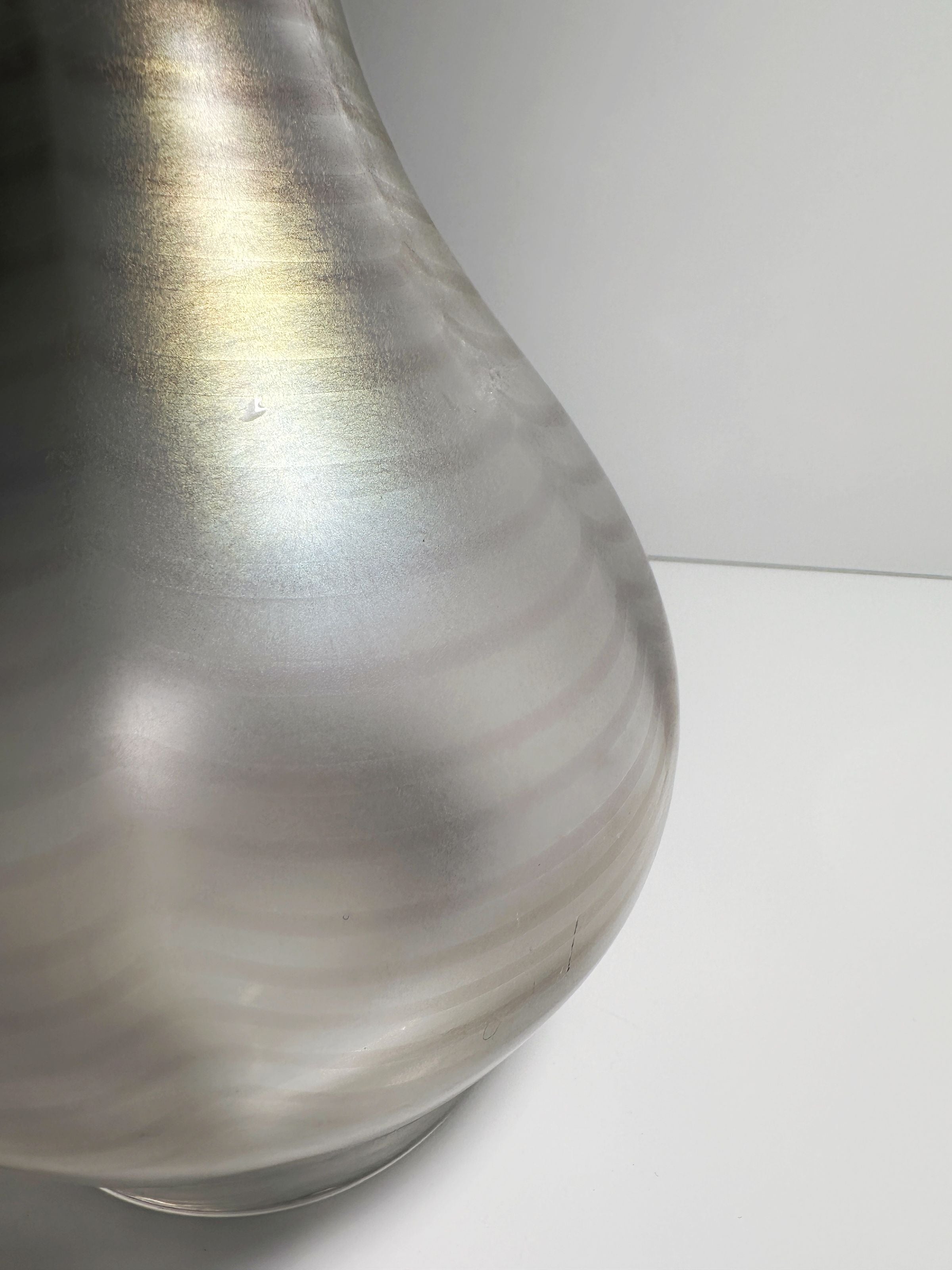 A close-up of the sleek Art Nouveau Wavy Vase from Dodo Vintage reveals its smooth metallic surface with subtle horizontal stripes. The vase's elegant curve is accentuated by soft lighting against a neutral backdrop, reminiscent of an iridescent glass masterpiece by Gallo.