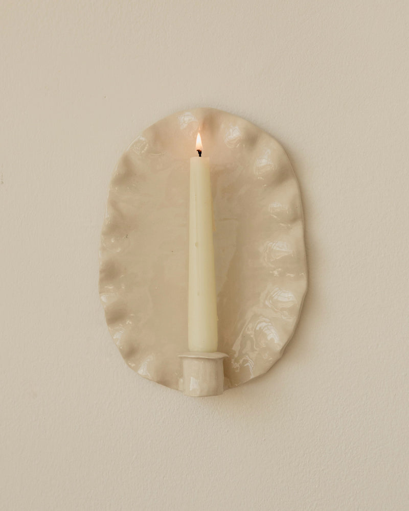 Lit taper candle in oval beige ceramic wall sconce holder