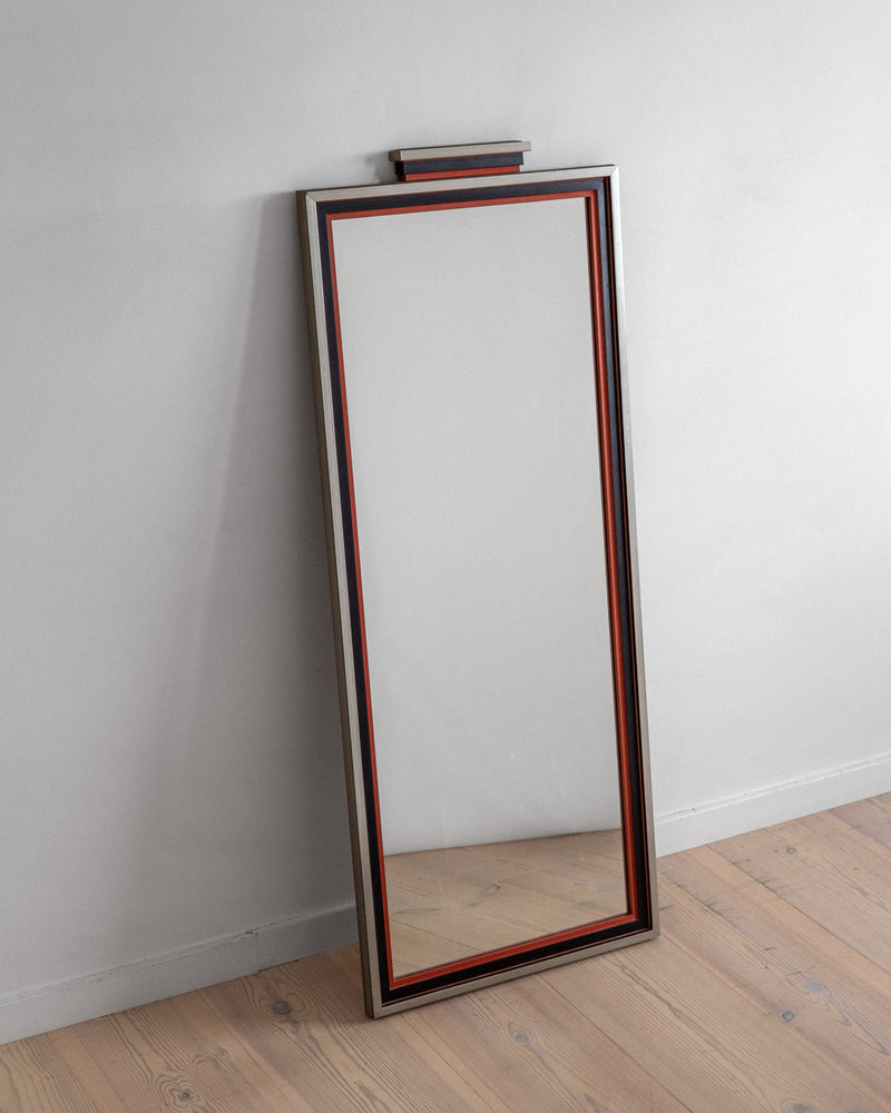A tall, rectangular Art Deco Mirror from Spigel, dating back to 1930s Sweden, features a thin red border and a wider silver frame. It leans against a light gray wall on a wood floor with visible grain patterns, capturing J.A. Edenholm's timeless design essence.
