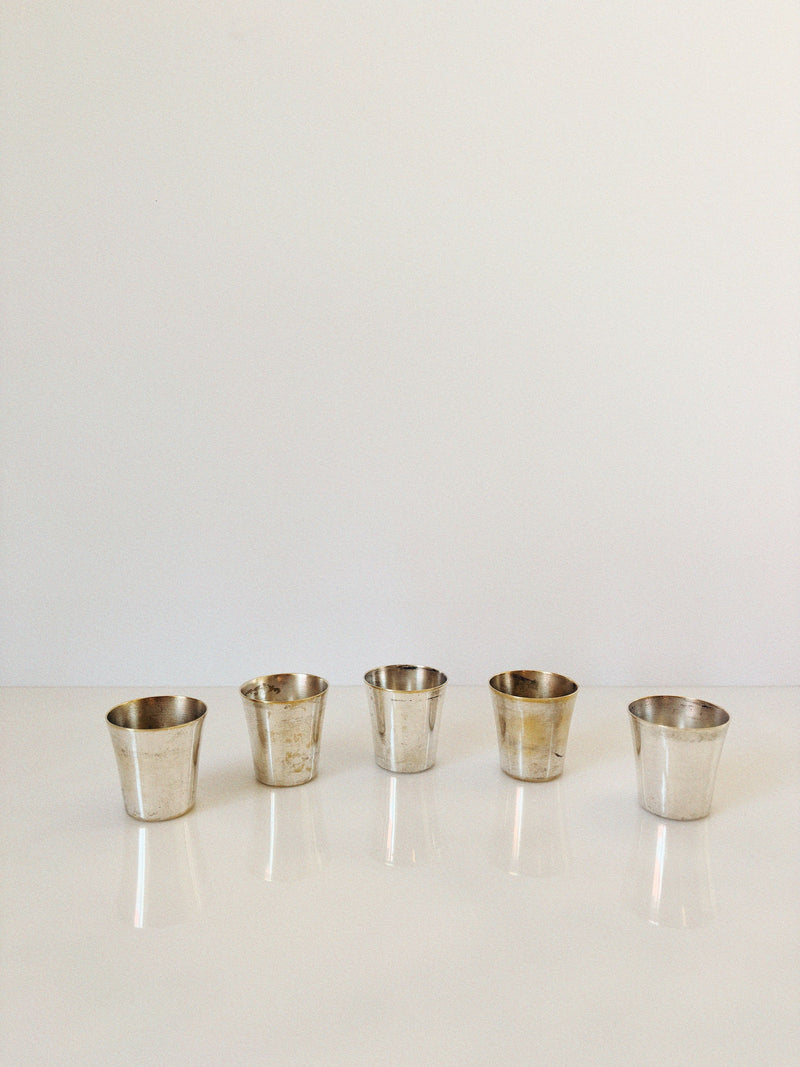 Five small, tarnished silver cups from the 60's Liquor Server Set by Imago Artis (Huerto) are evenly spaced in a row on a glossy white surface with a plain white background.