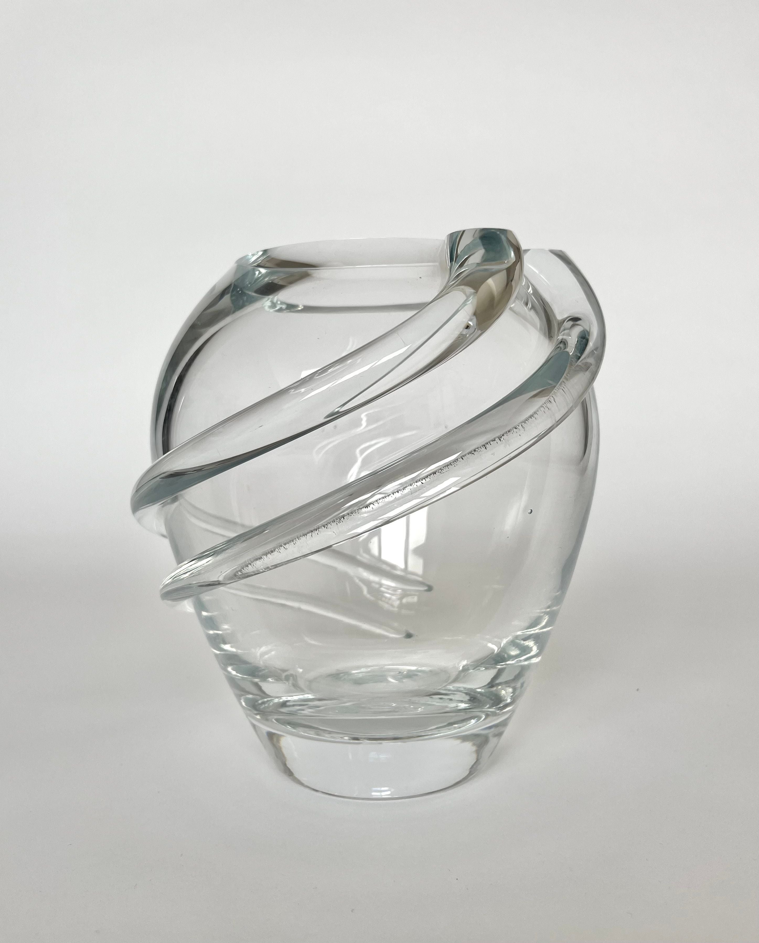 The Vintage Crystal Vase from septembre studios features an elegant oval shape and captivating swirl details, with two thick glass bands wrapped around its exterior. Set against a plain white background, this clear glass masterpiece exudes a timeless charm.