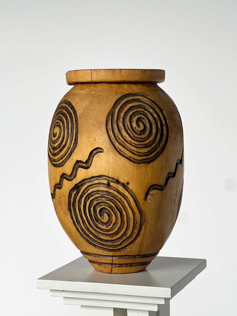Hand carved wooden vase with spiral motifs on white pedestal