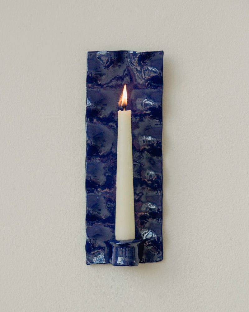 Blue glazed ceramic wall sconce with lit taper candle