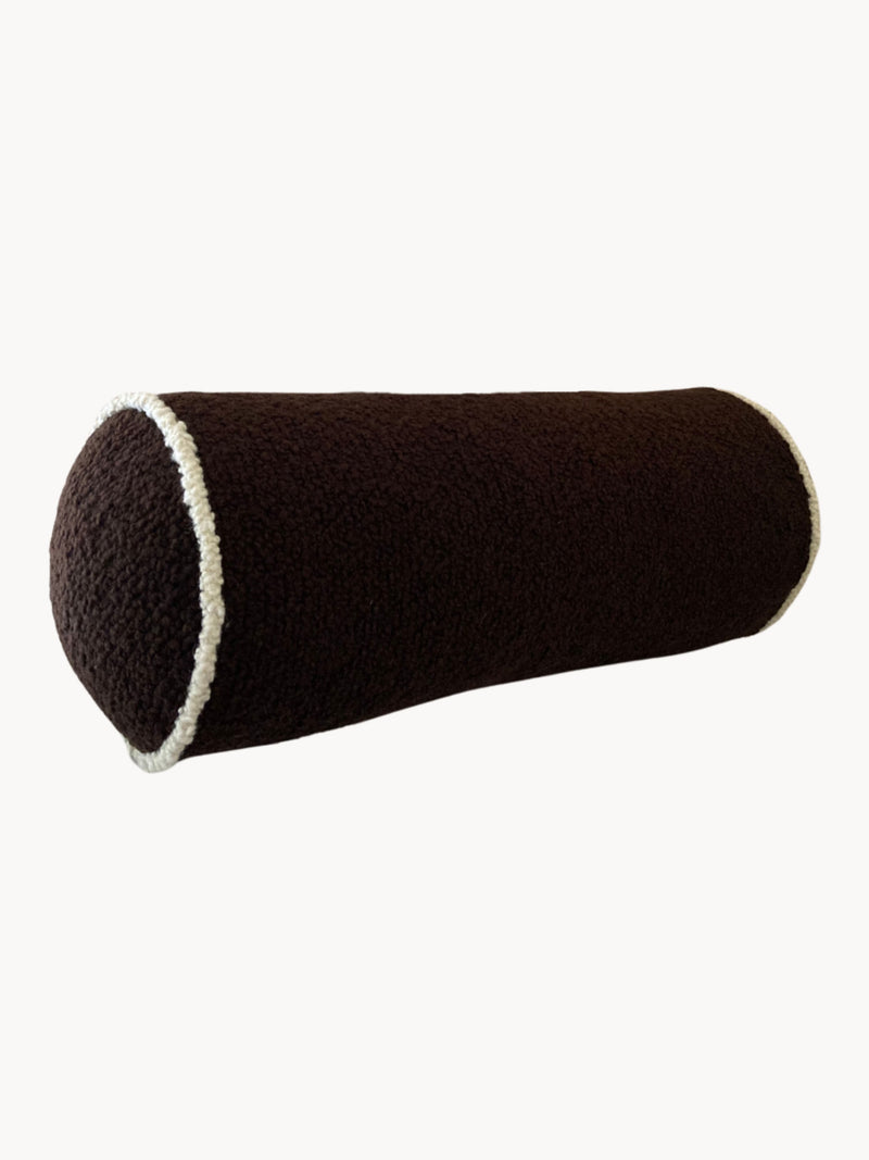 A cylindrical, dark brown bolster pillow with white trim on the ends. Crafted from luxurious wool bouclé fabric and handmade in the UK, its surface offers a soft, textured feel. The Le Cylindre - Passepoil - Wool Bouclé - Chocolate/Egg White by AMÉLIORÉ is showcased against a plain white background.