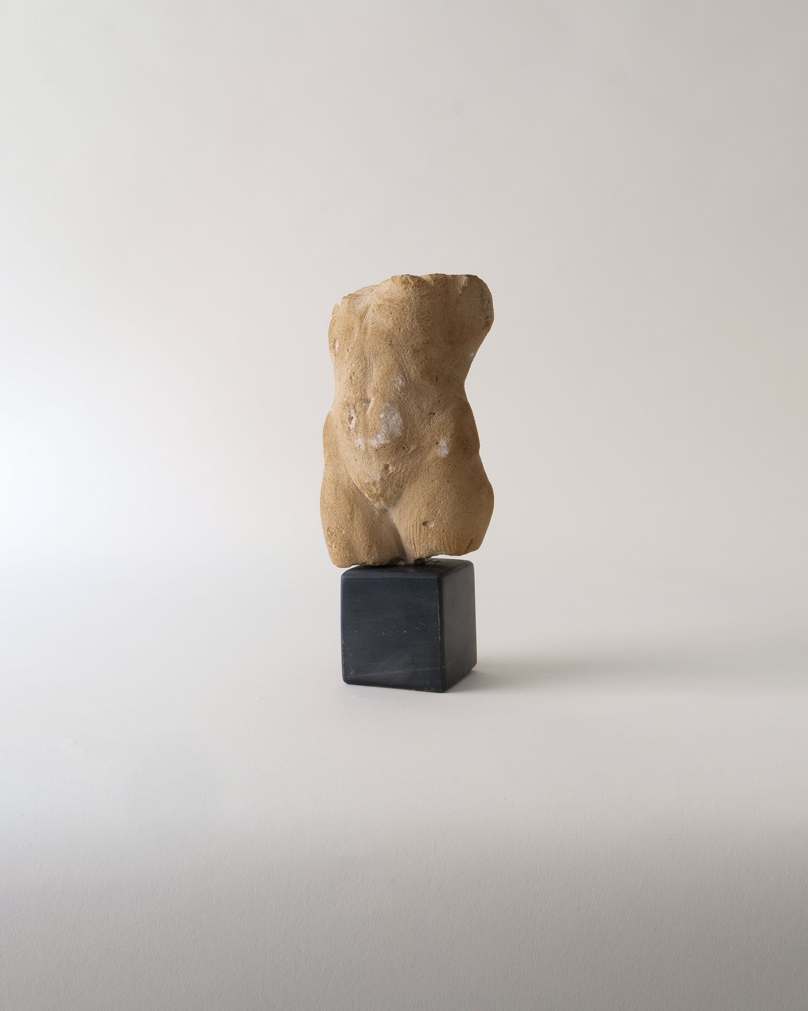 The Torso Sculpture by Misja Kristoffer Rasmussen (b.1971) from Collection apart features a rough, beige finish in classical style, resembling a human torso on a small dark base against a plain light gray background.