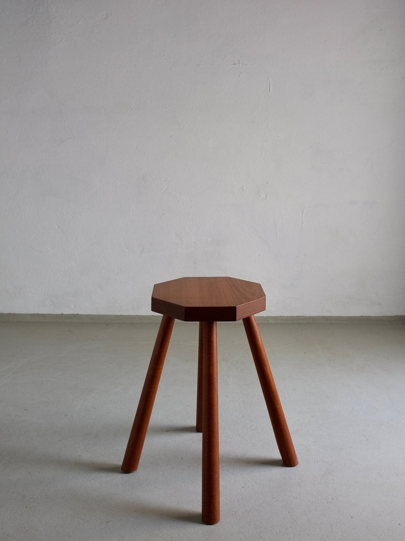 A vintage solid wood stool with an octagonal seat and four angled legs, known as the Solid Wood Octagonal Stool by Veter Vintage from Belgium in the 1960s, stands on a plain, light-colored floor against a blank, textured wall.