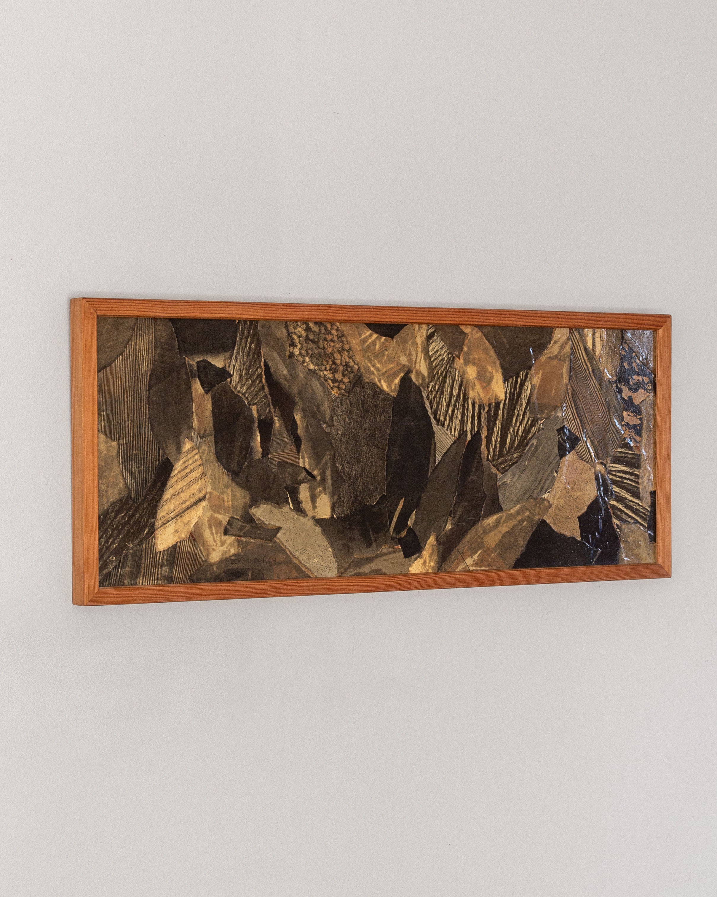 A rectangular wooden frame showcases the "Leaves" collage by Lars Bergander, combining dark, textured rock-like shapes on a light gray wall. This 1960s abstract piece from Sweden embodies depth and movement with mid-century modern Scandinavian art influences. Brand: Spigel.