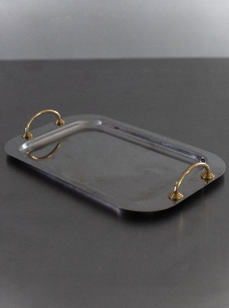 A rectangular, modern elegance Out For Lunch Stainless Steel Tray with two golden handles on either side. The tray features a smooth, reflective surface and is placed on a plain, dark background.