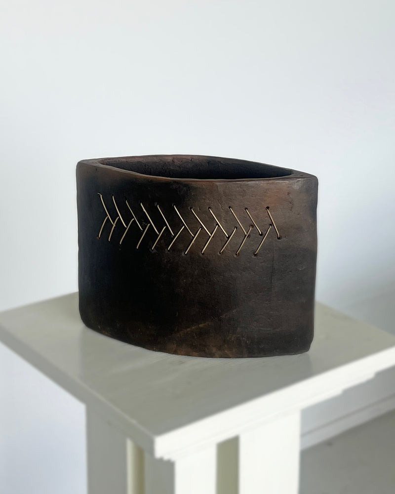 Dark terracotta vessel with golden geometric stitching pattern