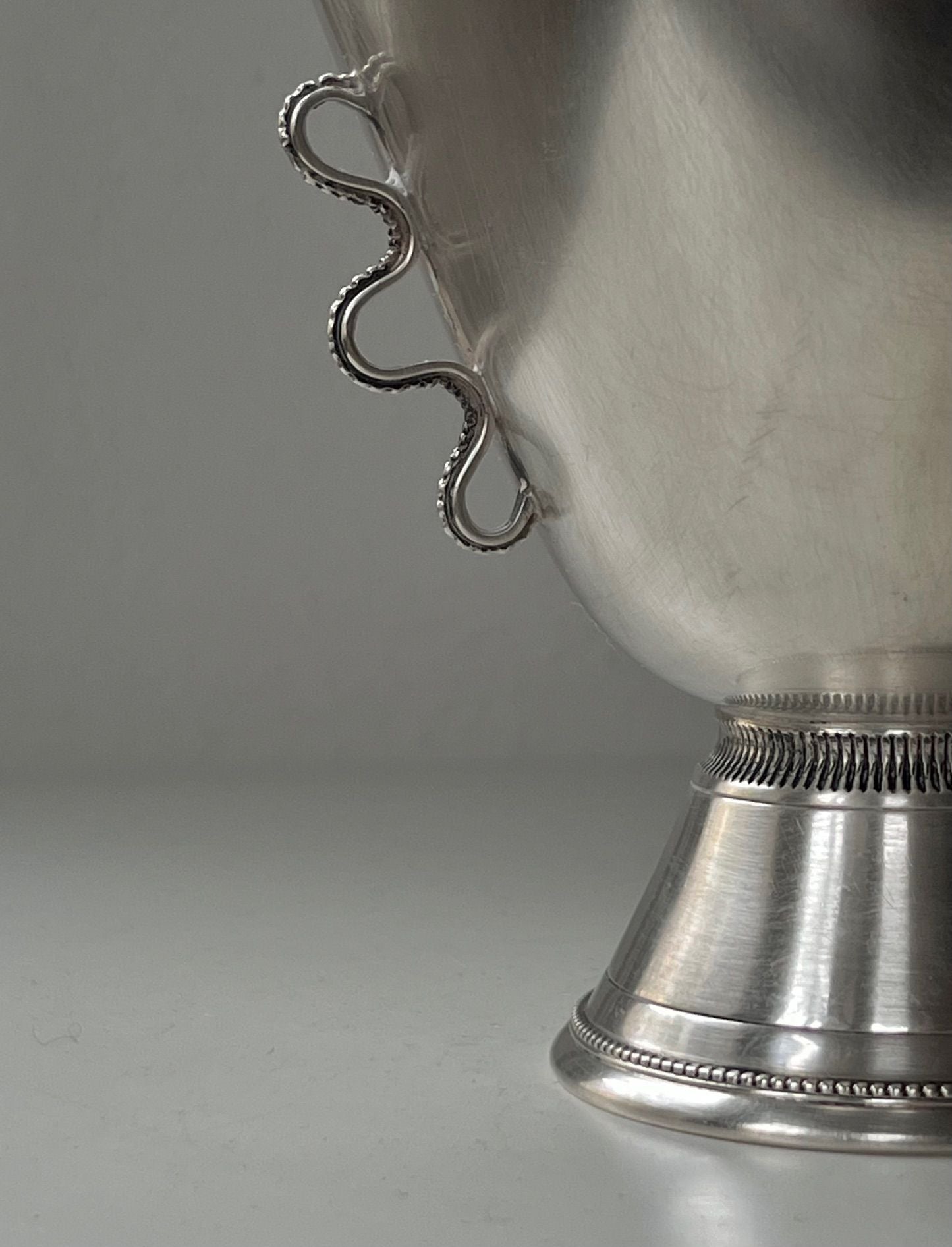 Close-up of an elegant hand-worked 1930s Silver Vase by Médecine, featuring ornate detailing on its handle and a decorative base. The polished surface subtly reflects light, reminiscent of a Stockholm artisan's craftsmanship.