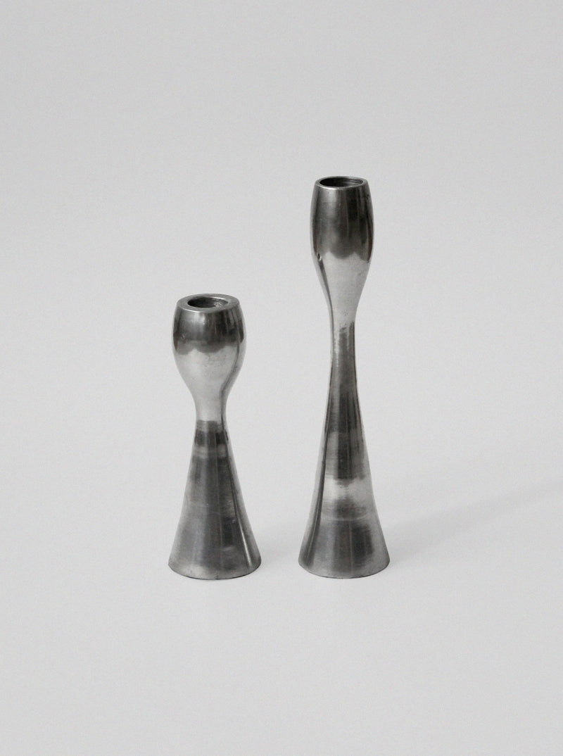 Two polished aluminum candleholders with sleek hourglass silhouettes