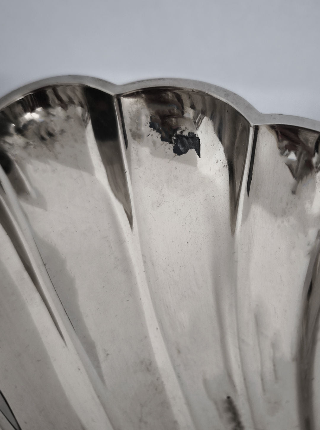 Close-up of Les Objoies' Shell Shape Vide-poches, a silver-plated item with a scalloped edge and polished, reflective surface. The smooth metal shows slight tarnish or chips.