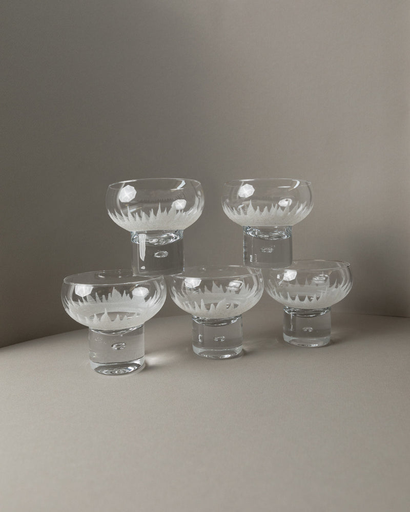 A set of five Bottega Jacobs wine and cocktail glasses from Italy (1970s) is arranged in a semicircle on a curved surface against a neutral background, casting soft shadows.