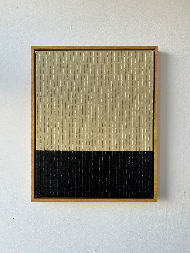 The framed "Buff Black - Oil on canvas" by Roi Elmaliah features a beige grid-textured top half and a black bottom half, reminiscent of Amsterdam's modern art scene, set against a plain white wall.