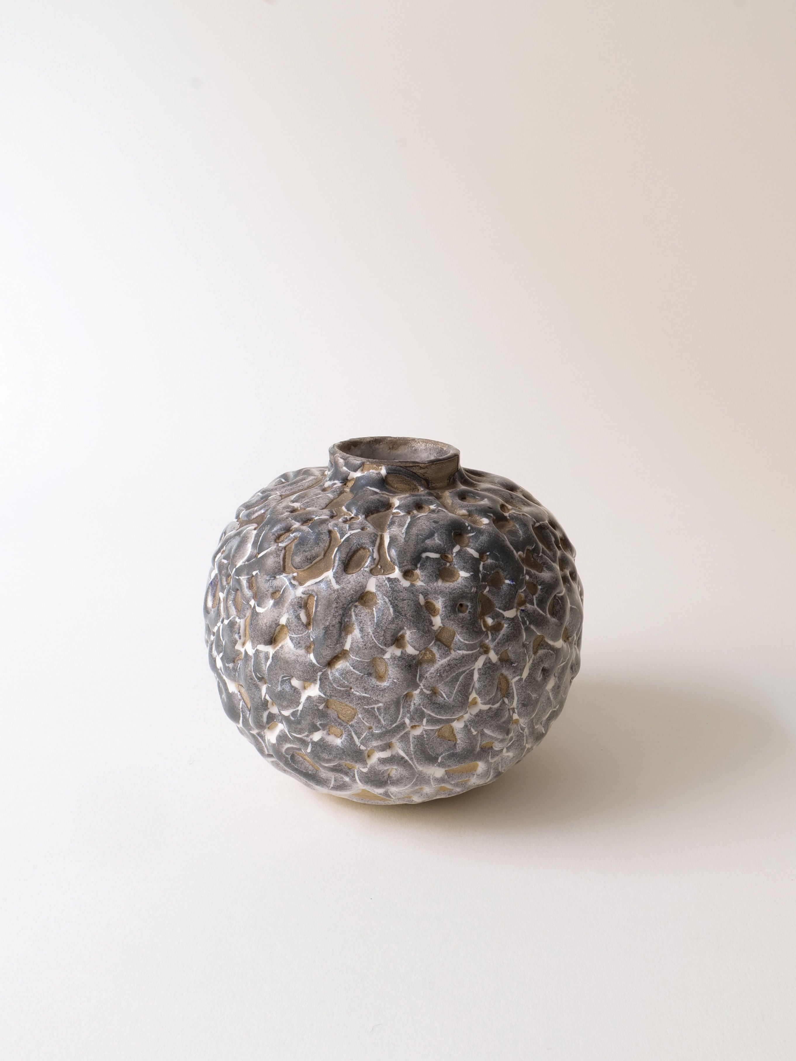 The Deco Ceramic Stem Vase 1930s by Collection apart is inspired by Alfred Renoleau, featuring a small textured round design with a narrow opening and an abstract uneven pattern in gray and blue atop a neutral stoneware ceramic backdrop.