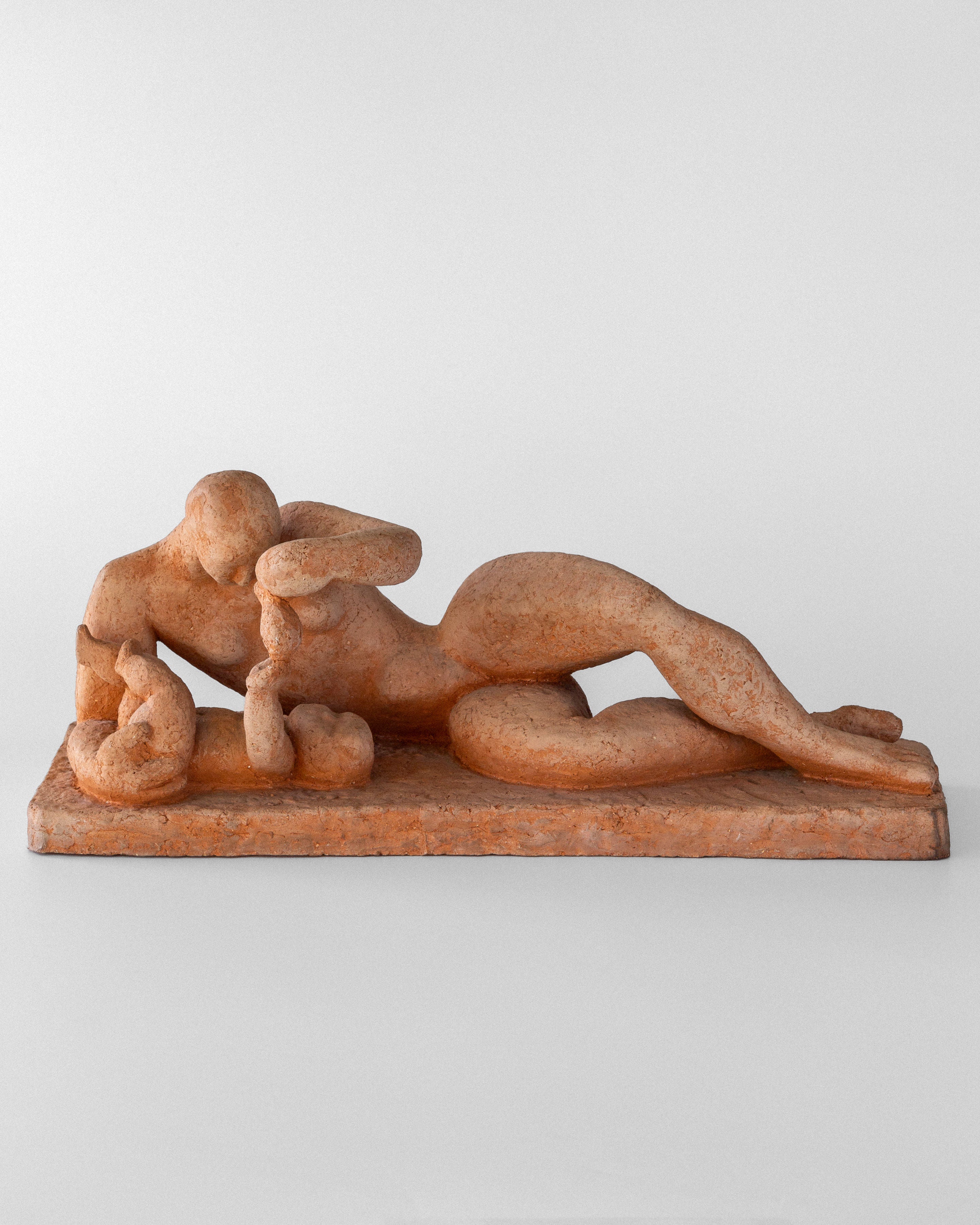 The unglazed terracotta sculpture "Modernist Terracotta Sculpture by Bengt Amundin" by Spigel features a reclining figure with an infant at her side, crafted in smooth, rounded forms on a rectangular base with a plain backdrop.