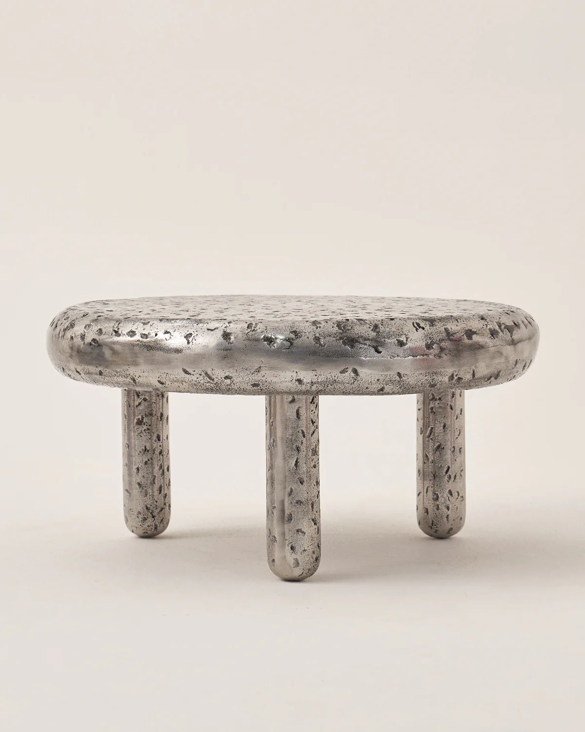 The Crater by LMNOH is a set of 2 small, round metallic stools with textured surfaces resembling lunar landscapes, featuring four short cylindrical legs.