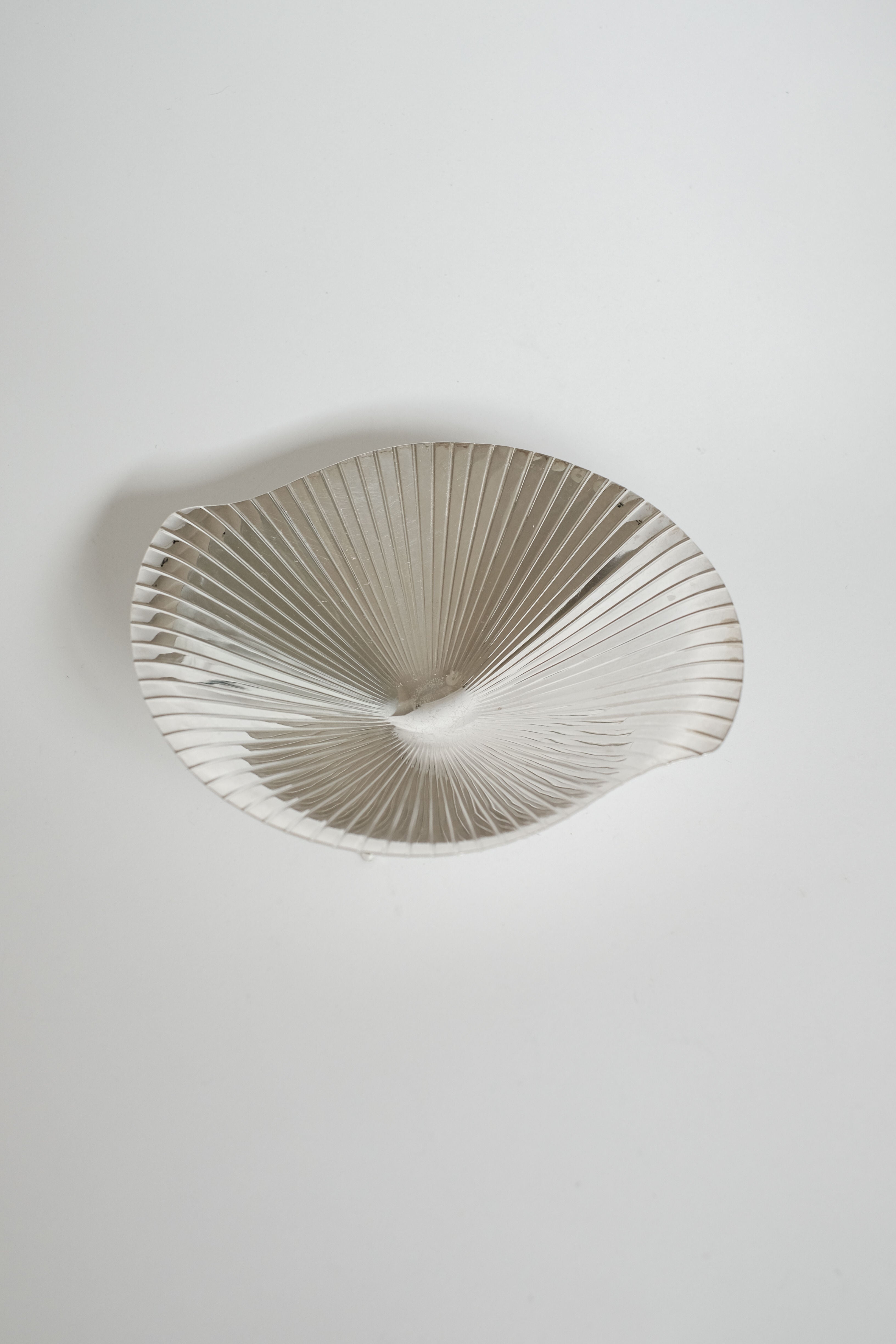 The Silverplated Shell Dish WMF by septembre studios features a fan-shaped, textured pleated design with irregular, wavy edges. Set against a plain white background, its reflective surface exudes vintage mid-century elegance.