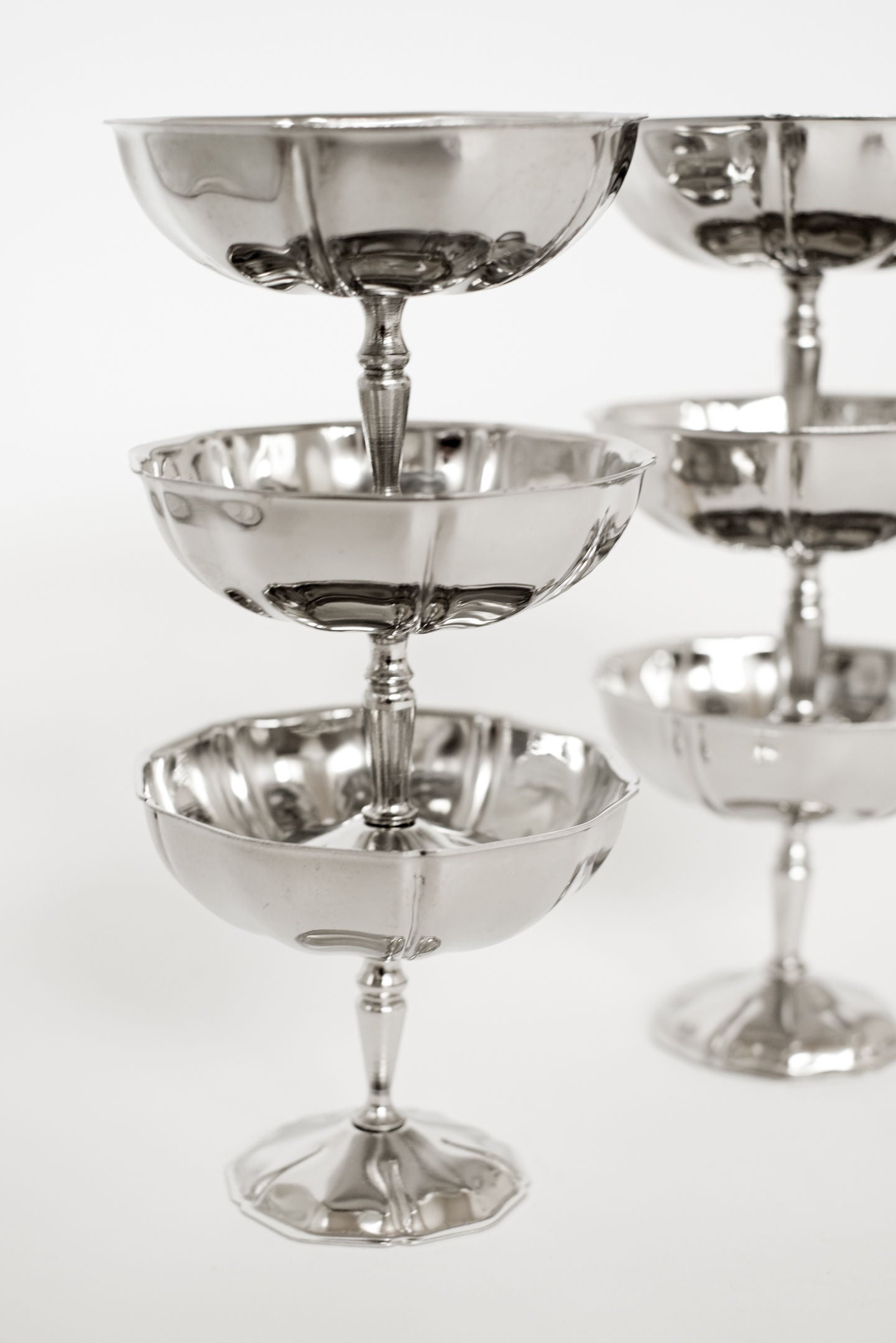 A close-up of the septembre studios Set of Six Ice Coupes, stacked in two tiers against a white backdrop. The empty stainless steel glasses shine elegantly, reflecting light and offering timeless vintage appeal.