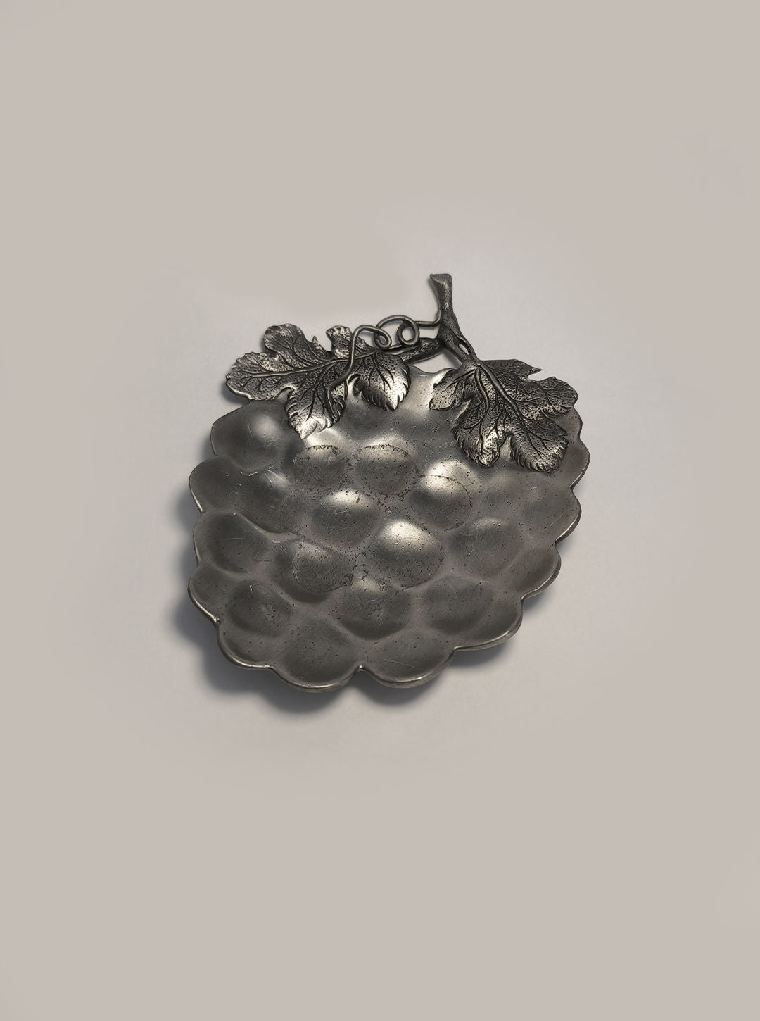 Introducing the Grape Vide Poches by Les Objoies—a pewter dish designed in the shape of a grape cluster. Adorned with intricately detailed grape leaves on a smooth background, this decorative piece elegantly embodies the enduring charm of a grapevine motif.