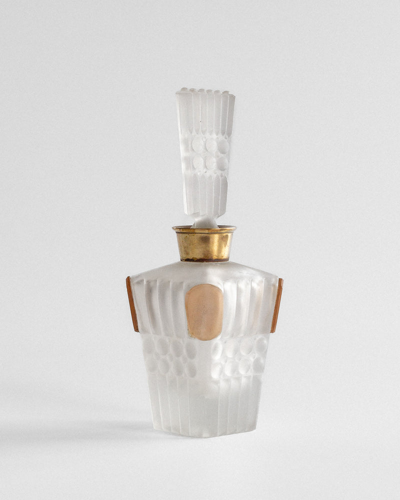 The Spigel Art Deco Perfume Bottle from 1930s France showcases frosted glass with a geometric ribbed design and elegant gold accents. Its tall, intricately shaped stopper enhances its sophistication, elegantly displayed on a neutral surface against a plain backdrop.