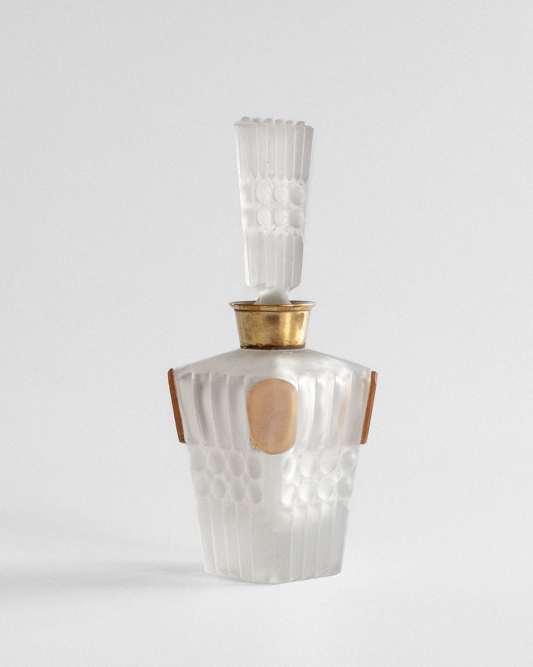 The Spigel Art Deco Perfume Bottle from 1930s France showcases frosted glass with a geometric ribbed design and elegant gold accents. Its tall, intricately shaped stopper enhances its sophistication, elegantly displayed on a neutral surface against a plain backdrop.