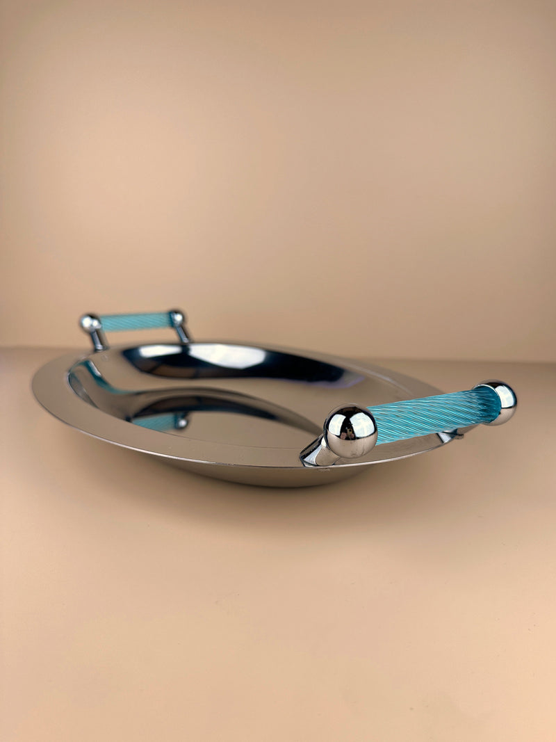 A sleek, oval-shaped silver-coloured metal tray with a polished finish and azure blue handles on each end is centered against a neutral beige background. The handles add a pop of color and texture to the minimalist design of this Italian 1980s Tray by Dodo Vintage.