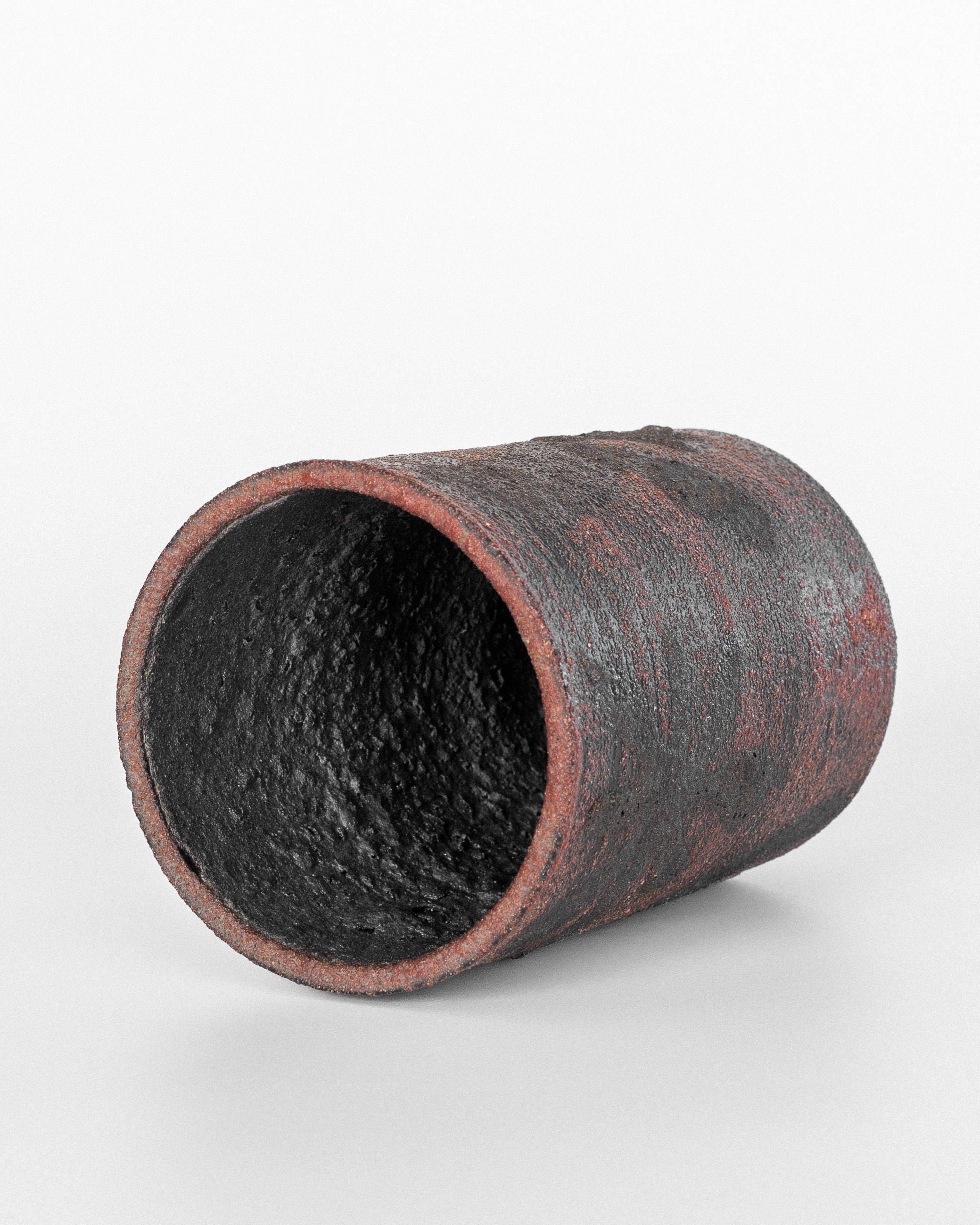 A rust-colored, cylindrical ceramic object by Spigel brand Dutch ceramicist Jaap Dommisse rests on its side against a white background, its textured surface and rough interior enhancing the modernistic appeal as it tilts slightly toward the viewer.