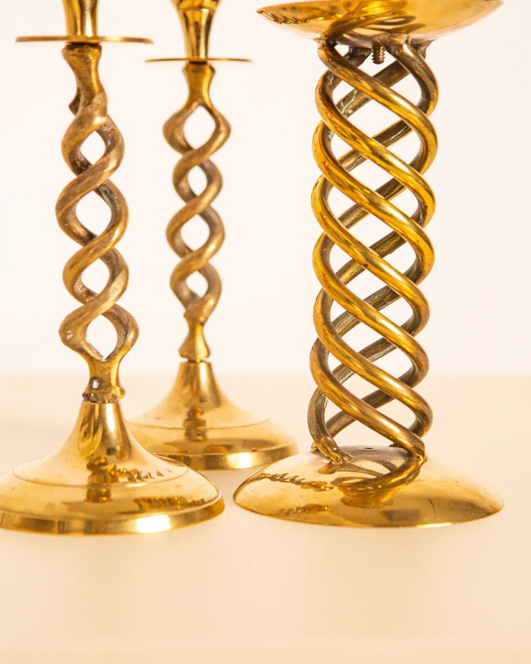 The Treaptyque Set of 3 Italian 60's Gilded Metal Candleholders, featuring intricate twisted spiral designs, elegantly stand on a smooth surface against a soft, neutral background, showcasing craftsmanship that combines elegance and artistry.