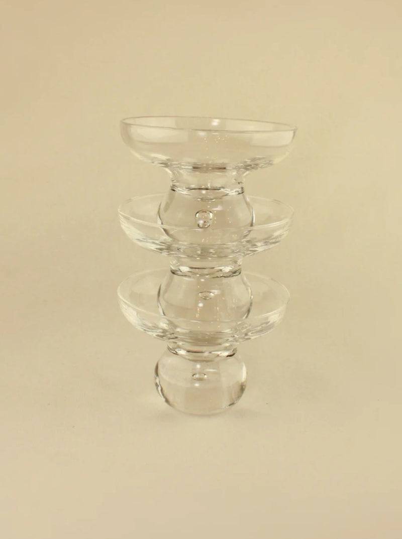 A clear glass sculpture featuring three stacked rounded bowls of decreasing size from bottom to top, reminiscent of vintage crystal glasses. The design is minimalist and symmetrical, standing against a neutral beige background. Introducing Italian Glasses by Boga Avante Shop.