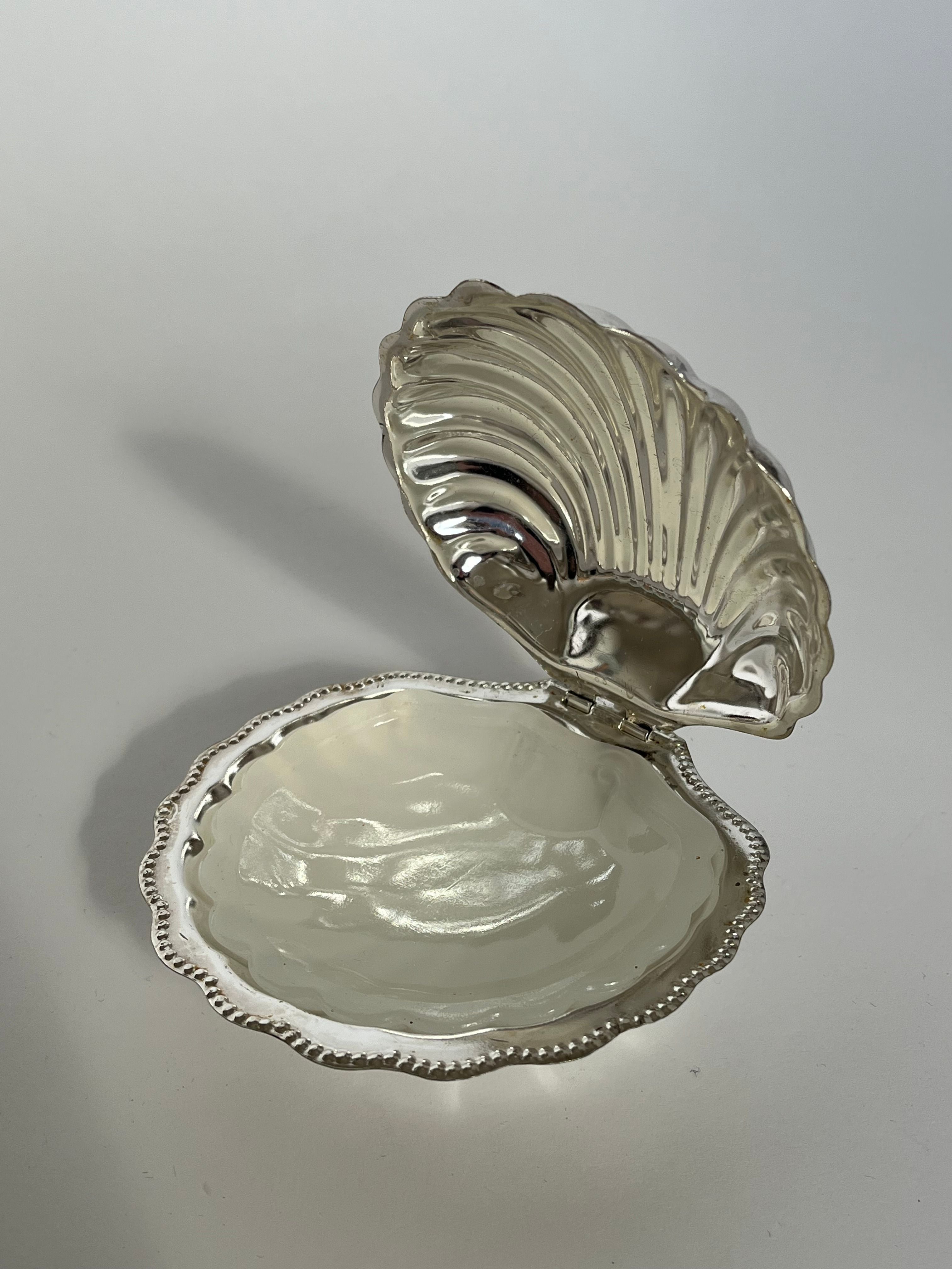 An elegant Shell Shaped Butter Dish by septembre studios, crafted from vintage brass and featuring decorative edges, is displayed open to reveal its smooth interior. The plain light gray background accentuates the intricate design and shiny surface of this sophisticated piece.