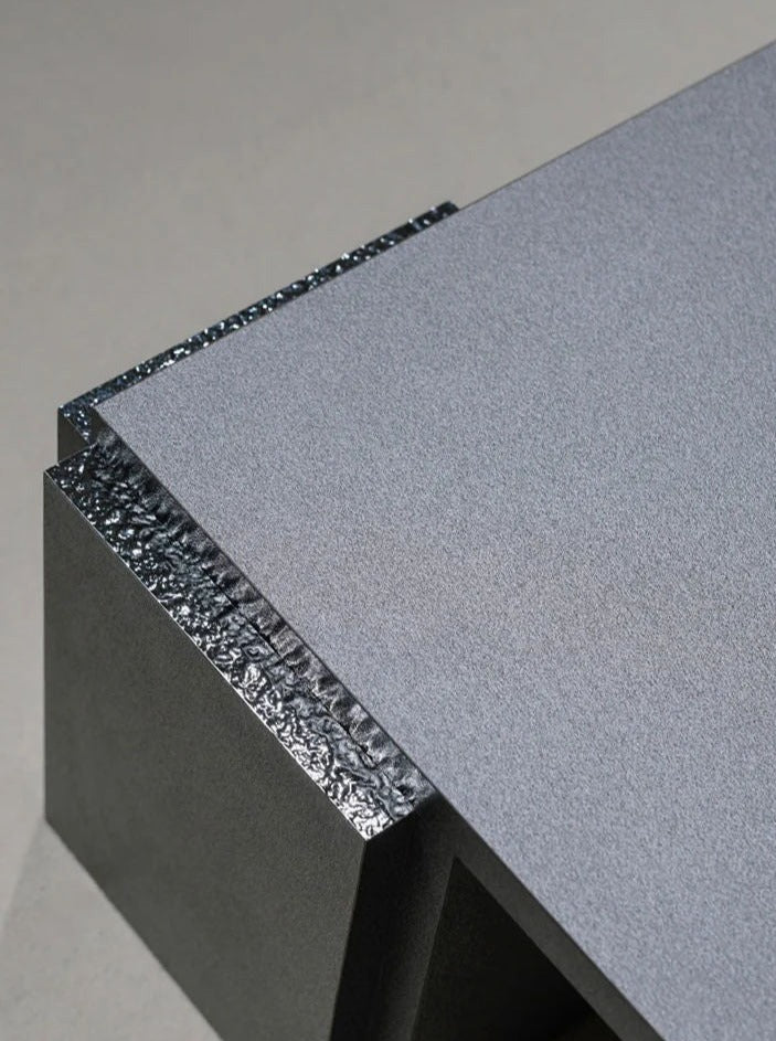 A close-up of a contemporary, angular sculpture featuring textured metallic sections and smooth surfaces, reminiscent of the "Mara" Coffee Table – Night Noise by TEGET. The piece showcases sharp-edged structures and contrasting textures, emphasizing its industrial aesthetic and minimalist design.